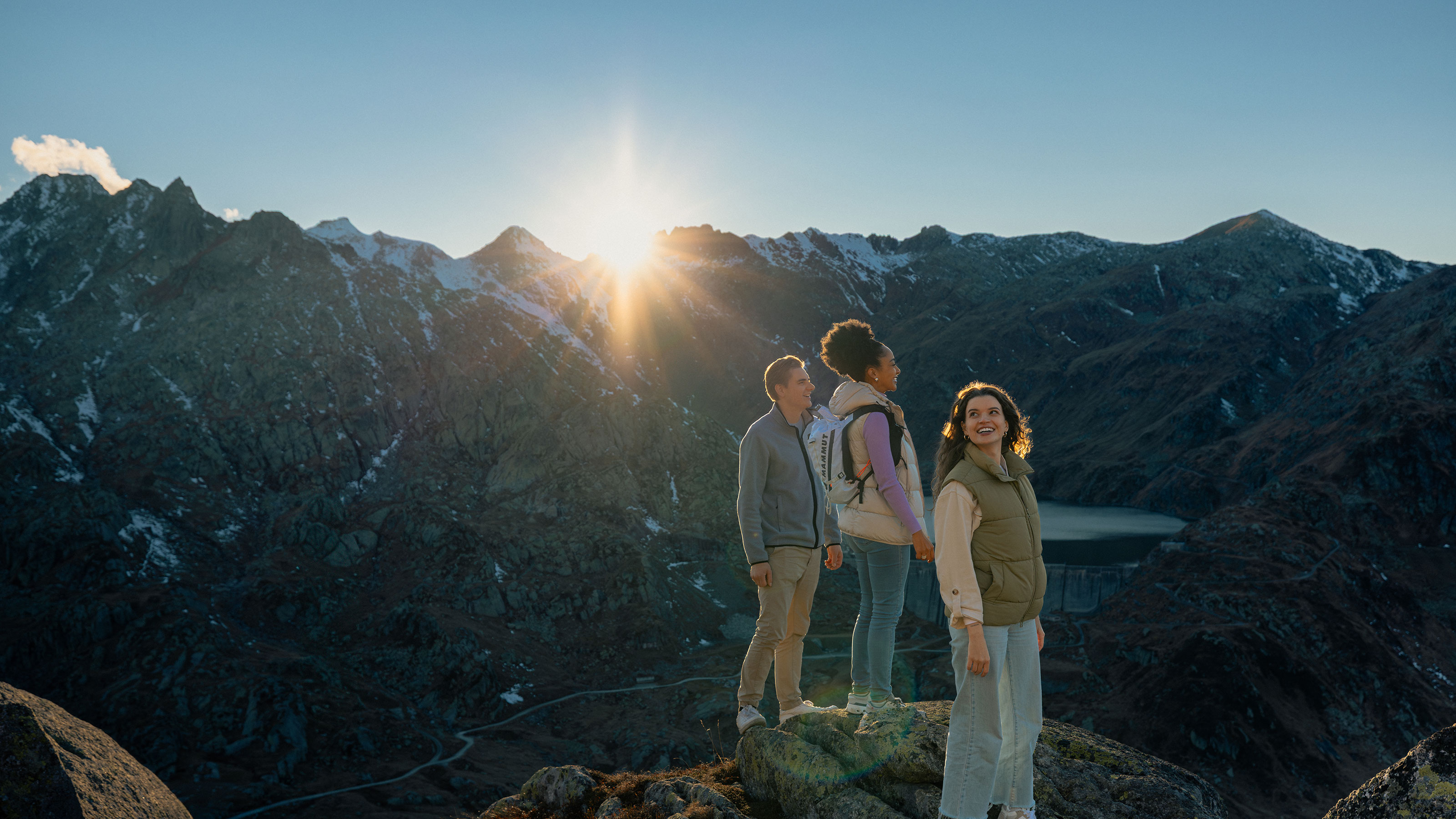 Drei junge Personen stehen auf Felsen mit Blick auf die beeindruckende Berglandschaft.