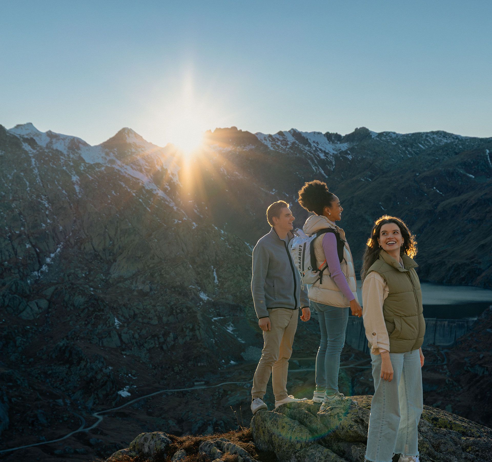 Drei junge Personen stehen auf Felsen mit Blick auf die beeindruckende Berglandschaft.