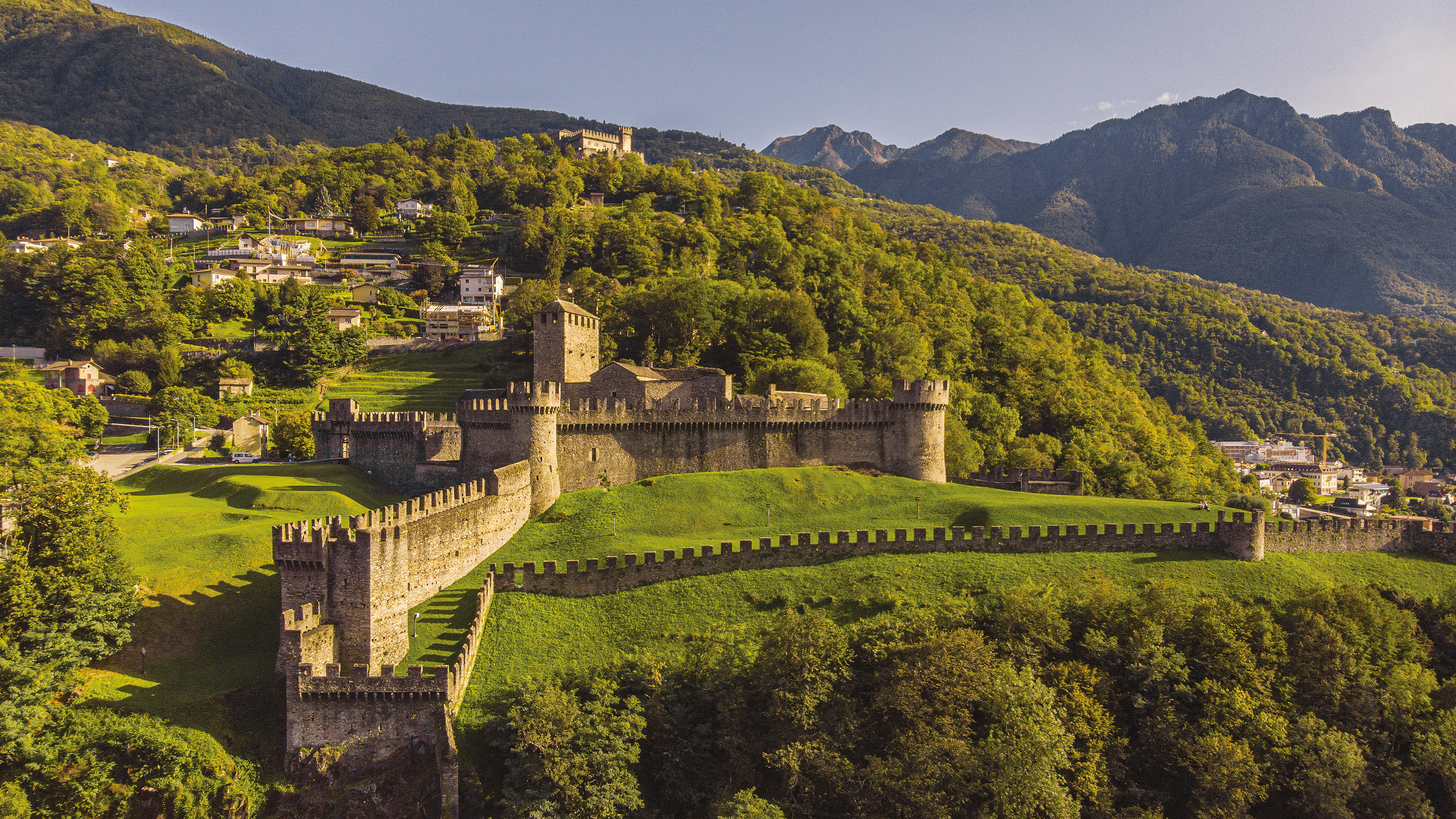 A castle on a forested hill with mountains.