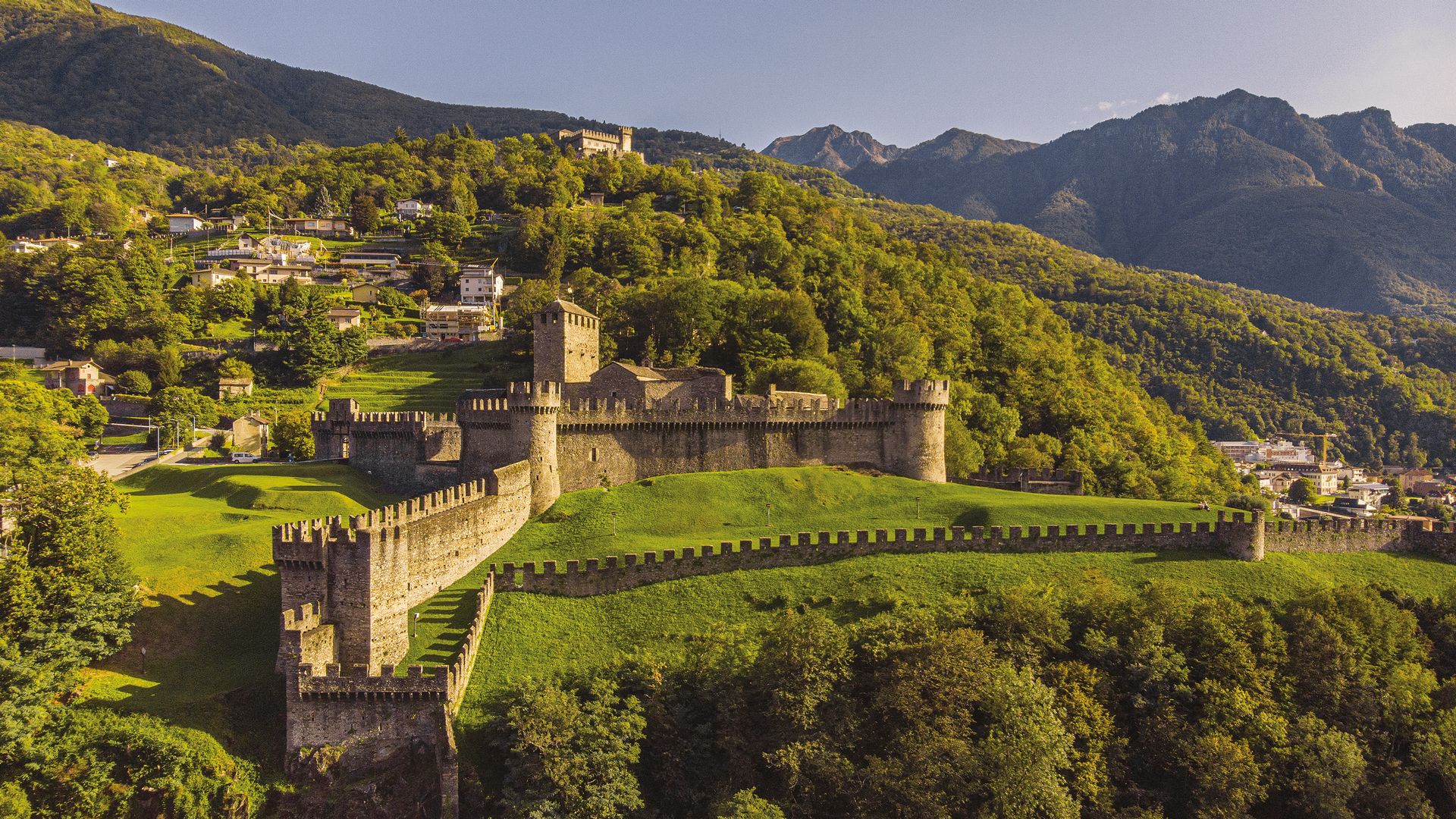 Un château sur une colline boisée avec des montagnes.