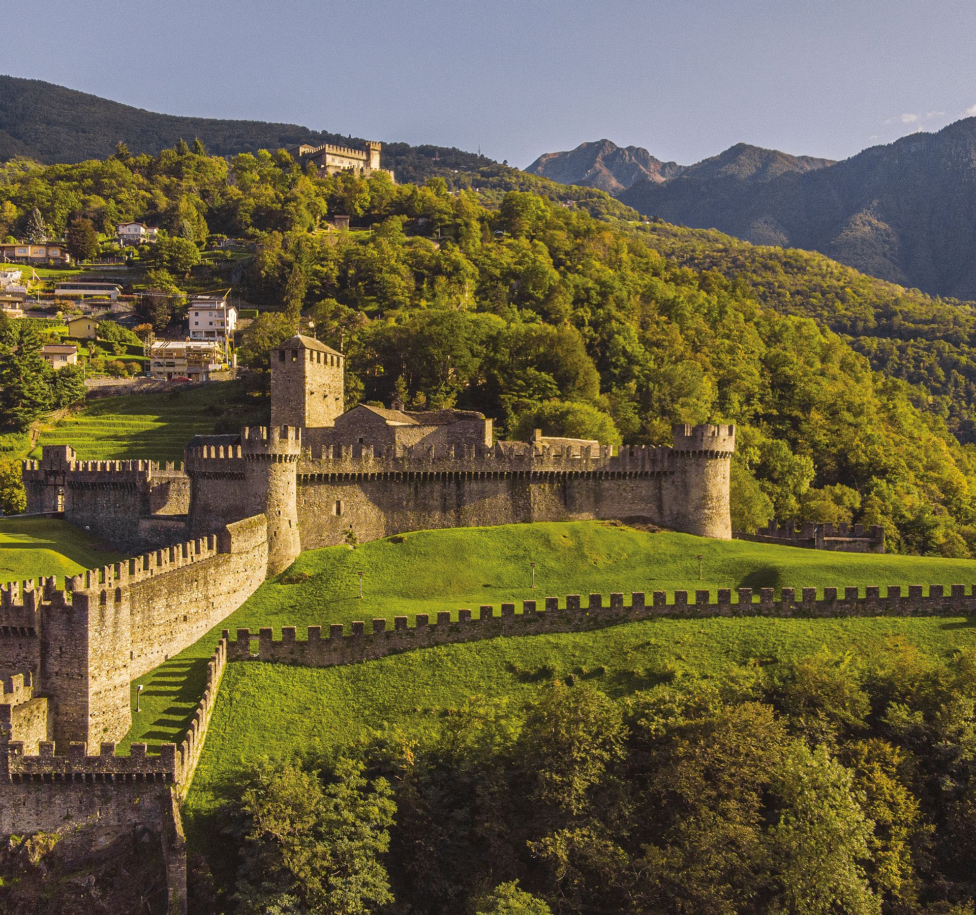 Eine Burg auf einem bewaldeten Hügel mit Bergen.