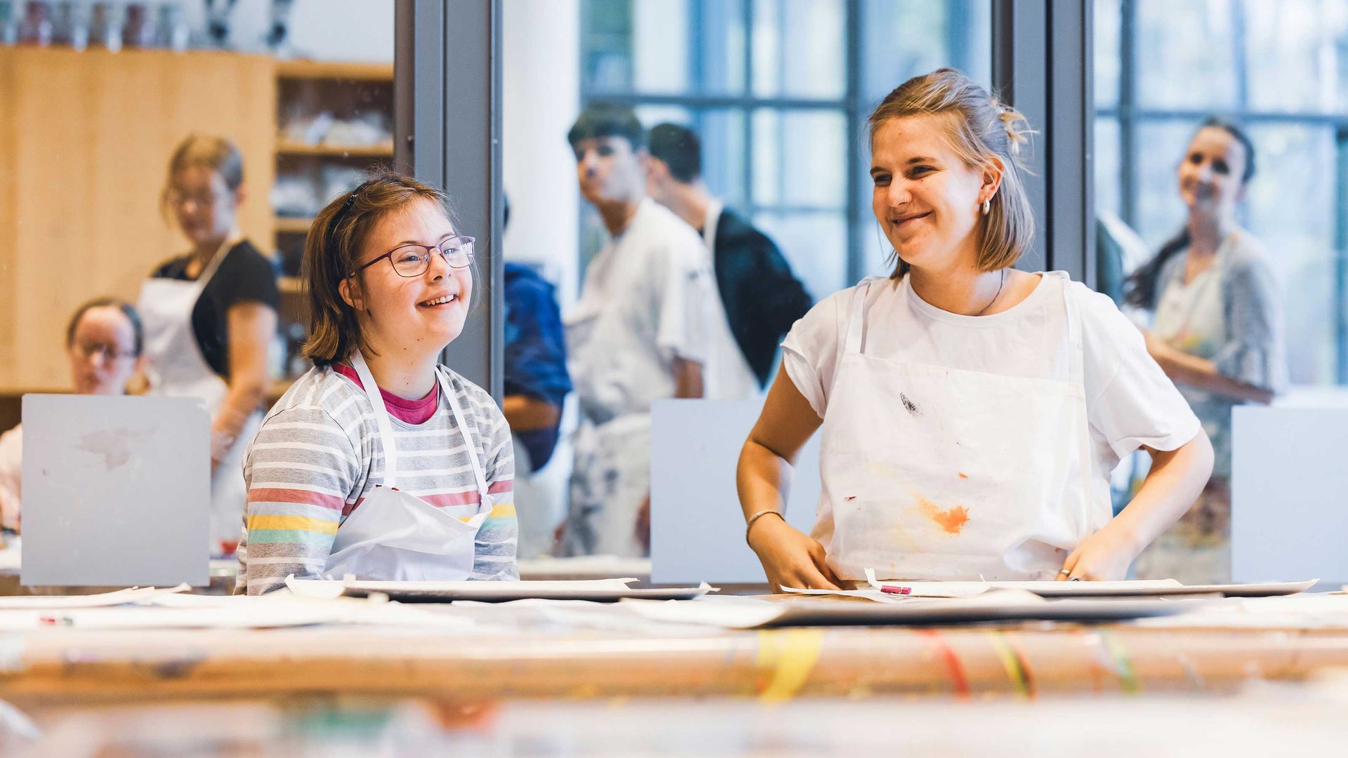 Due ragazze della classe di arte si sorridono a vicenda mentre sono circondate da materiale artistico colorato.