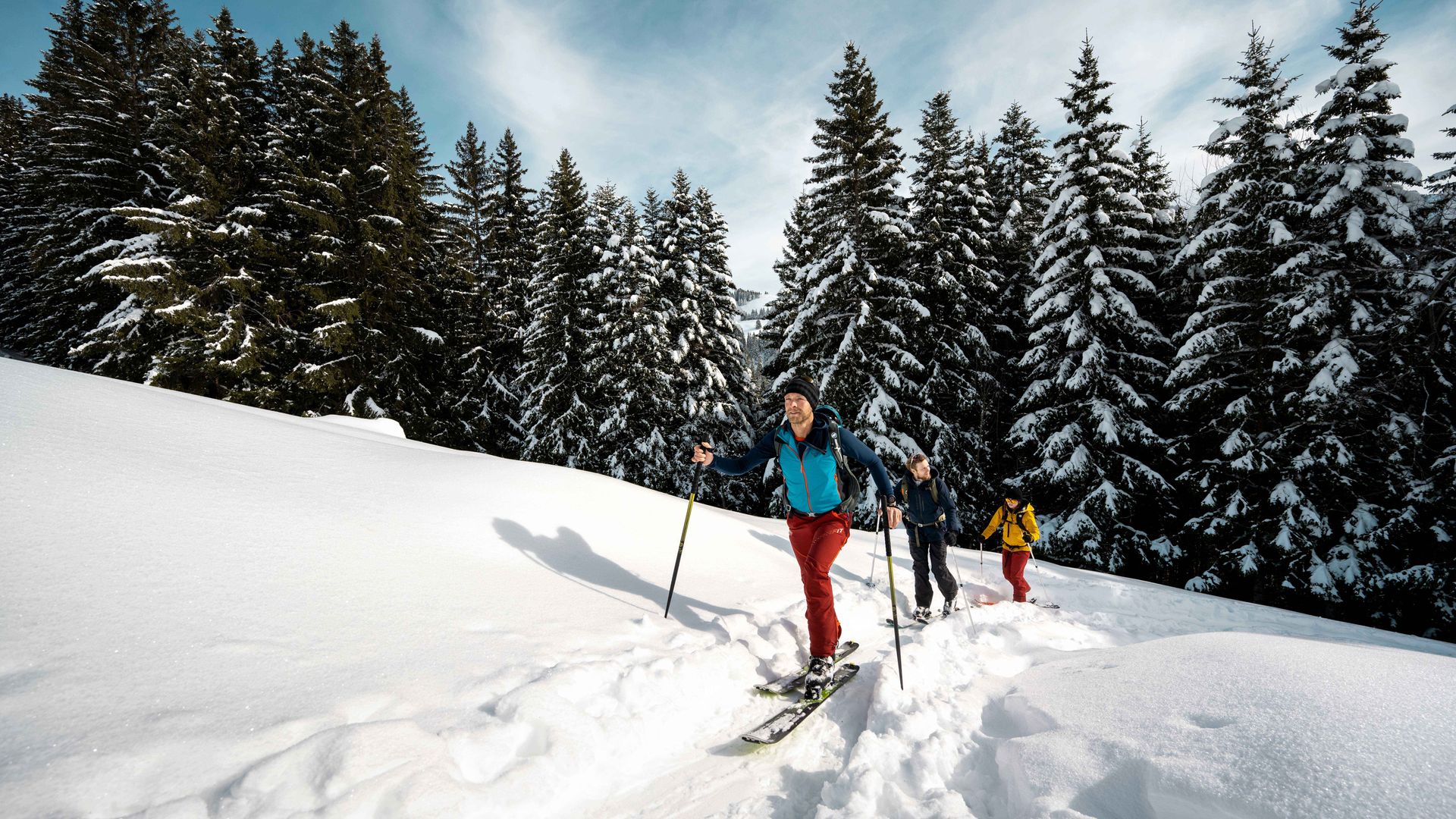 Trois personnes skient sur une piste enneigée dans un paysage hivernal tranquille.