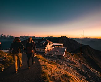 Zwei Wanderer steigen während des Sonnenuntergangs auf einen Berg und werfen lange Schatten auf das felsige Gelände.
