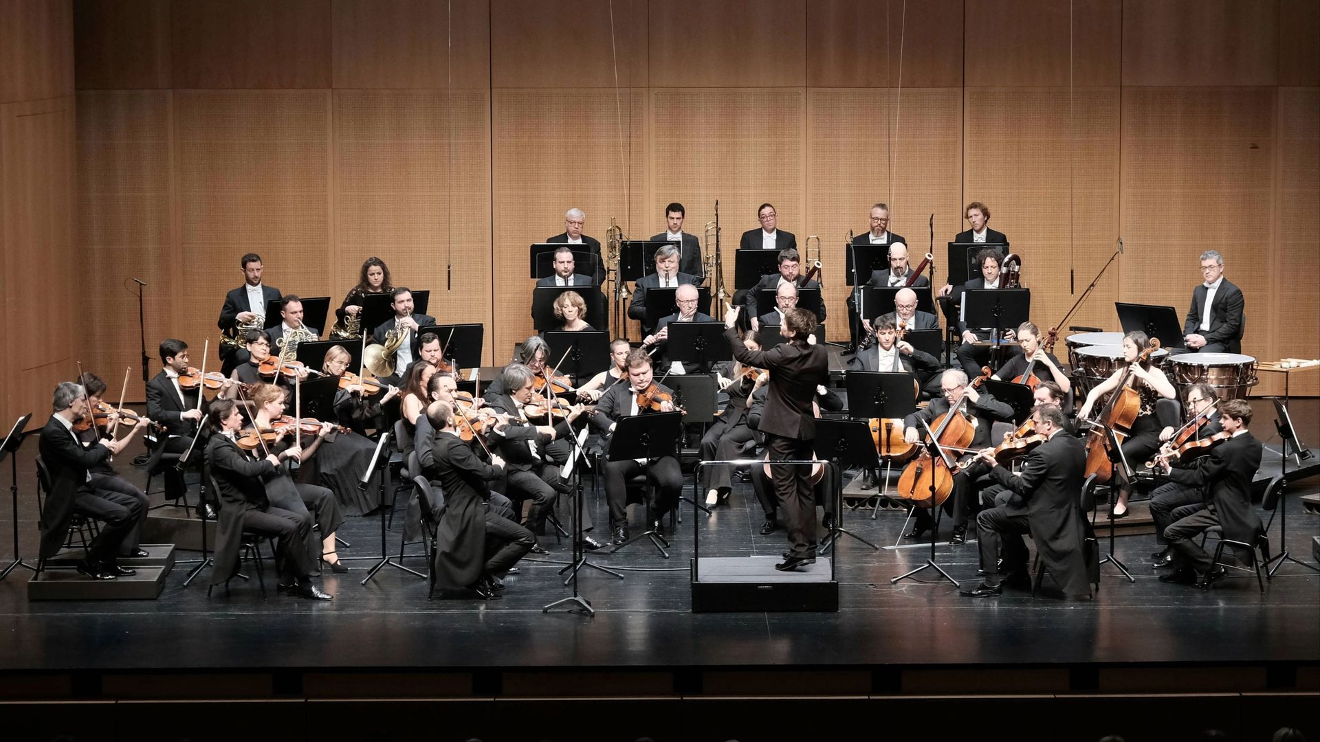 L’Orchestra della Svizzera italiana in concerto, musicisti sul palco con i loro strumenti, diretti dal direttore d’orchestra.