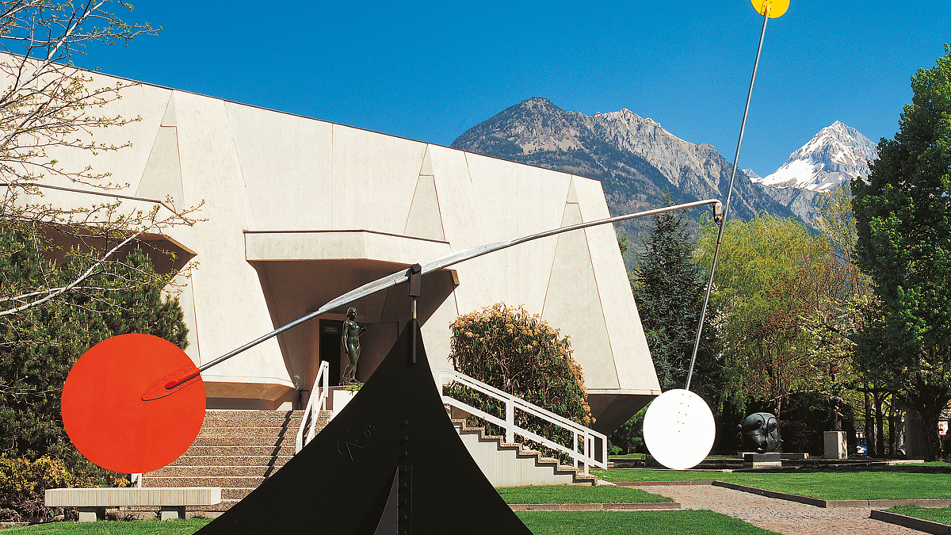 A sculpture in a garden in front of a building with a mountain in the background