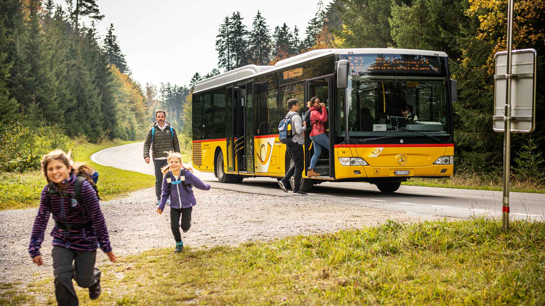 A group of children joyfully running down a road beside a parked bus, capturing a moment of carefree playfulness.