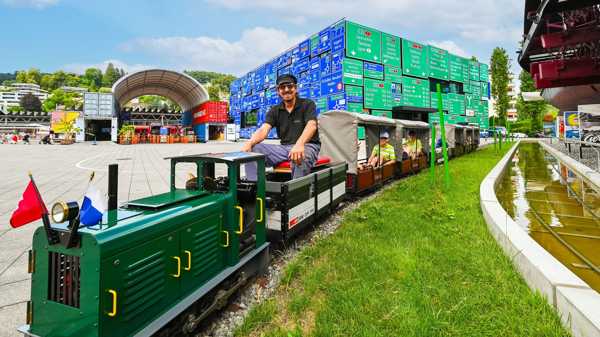 Miniature railway with green train and several open carriages, staffed with children, on tracks on the premises of the Swiss Museum of Transport.
