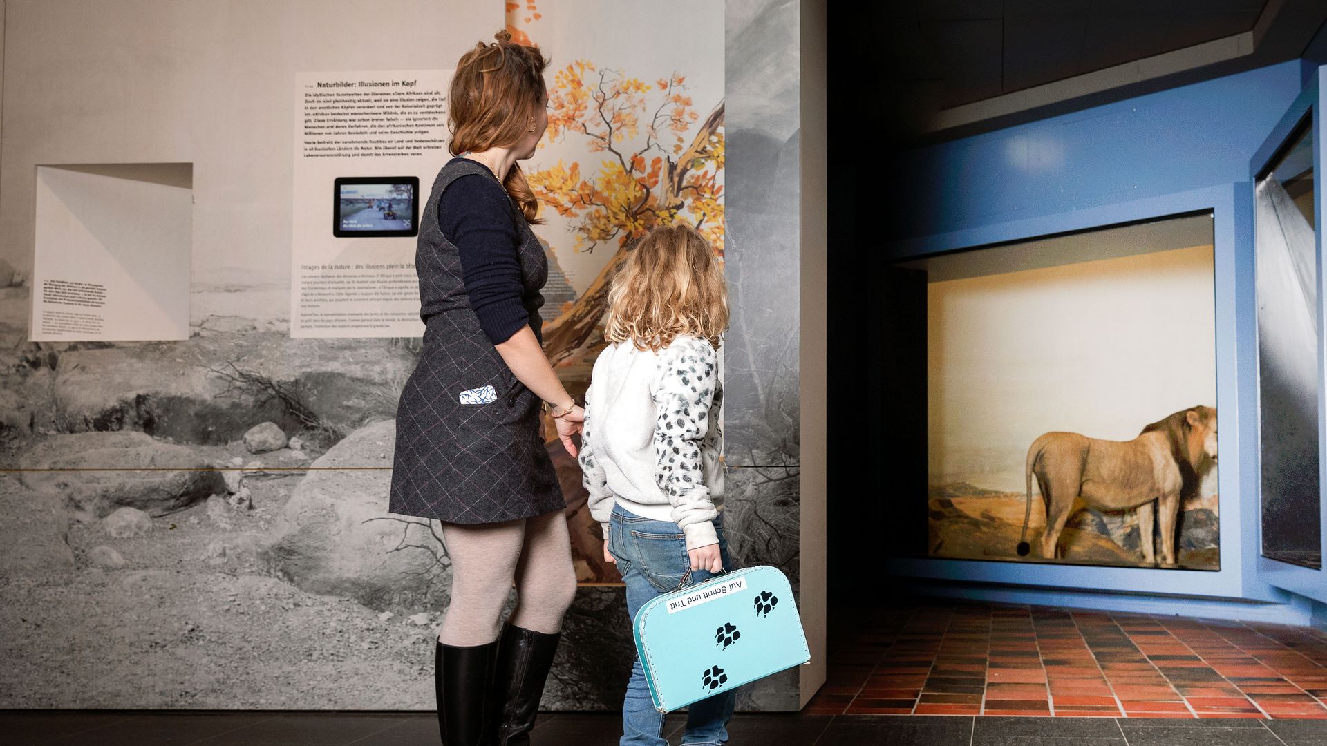 Femme et enfant regardant une vitrine avec un lion, un diorama et un graphique mural au Musée d'histoire naturelle de Berne.