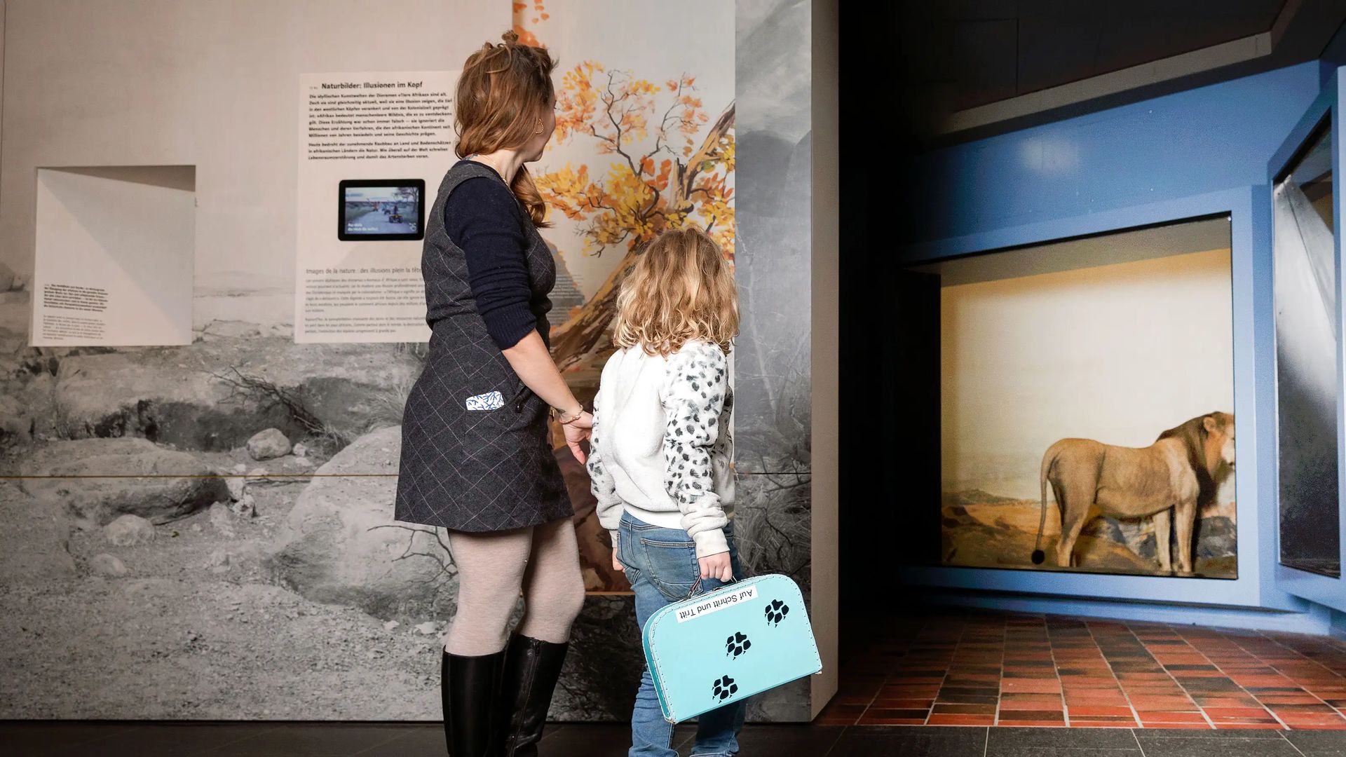 Woman and child looking at a lion display case with diorama and wall graphic at the Natural History Museum Bern.