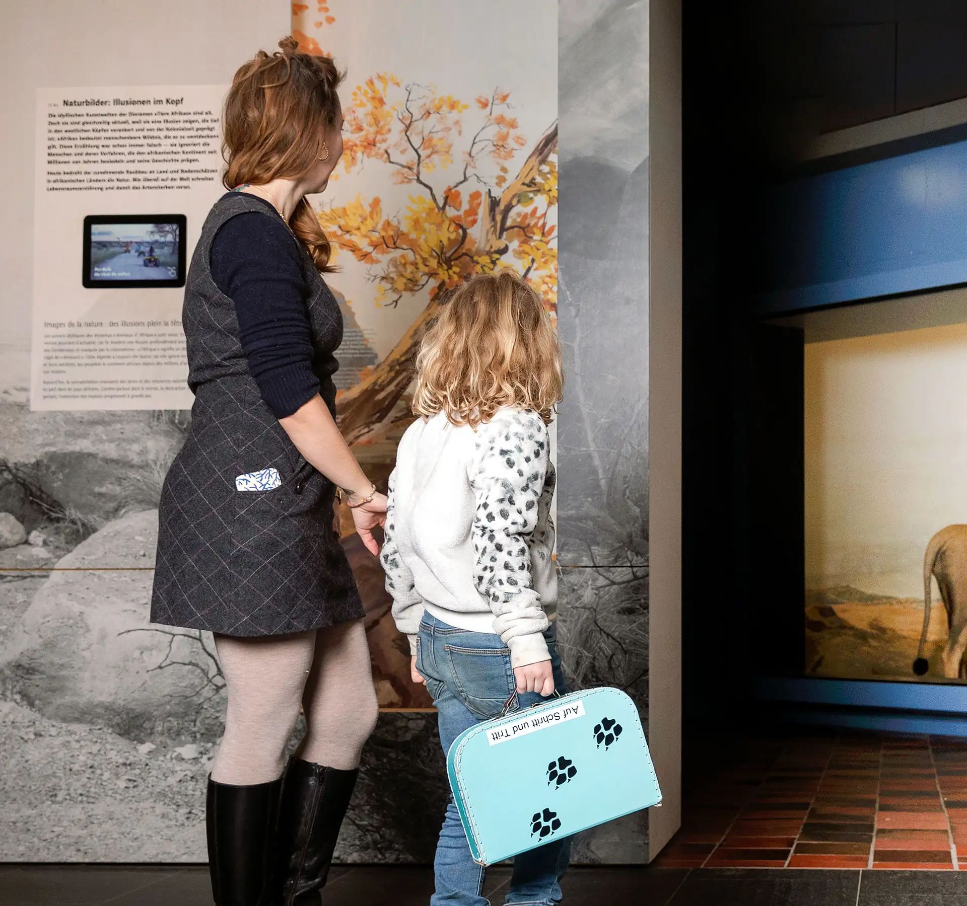 Woman and child looking at a lion display case with diorama and wall graphic at the Natural History Museum Bern.