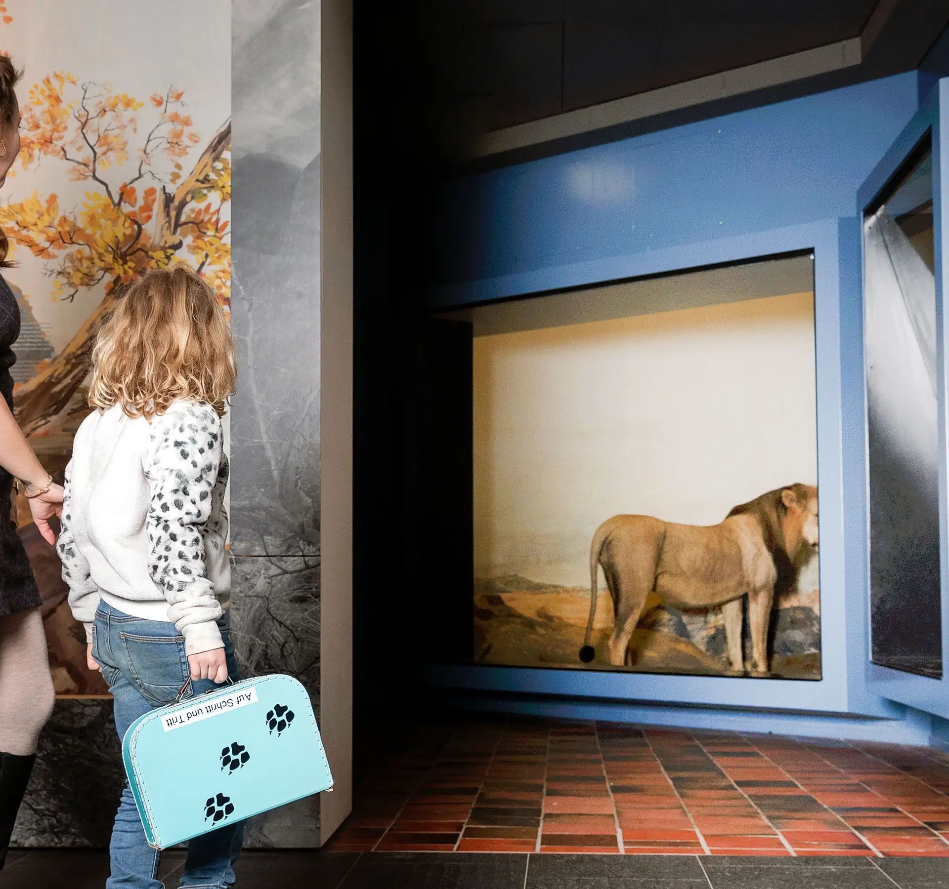 Donna e bambina osservano una teca con un leone, un diorama e una grafica murale al Museo di storia naturale di Berna.