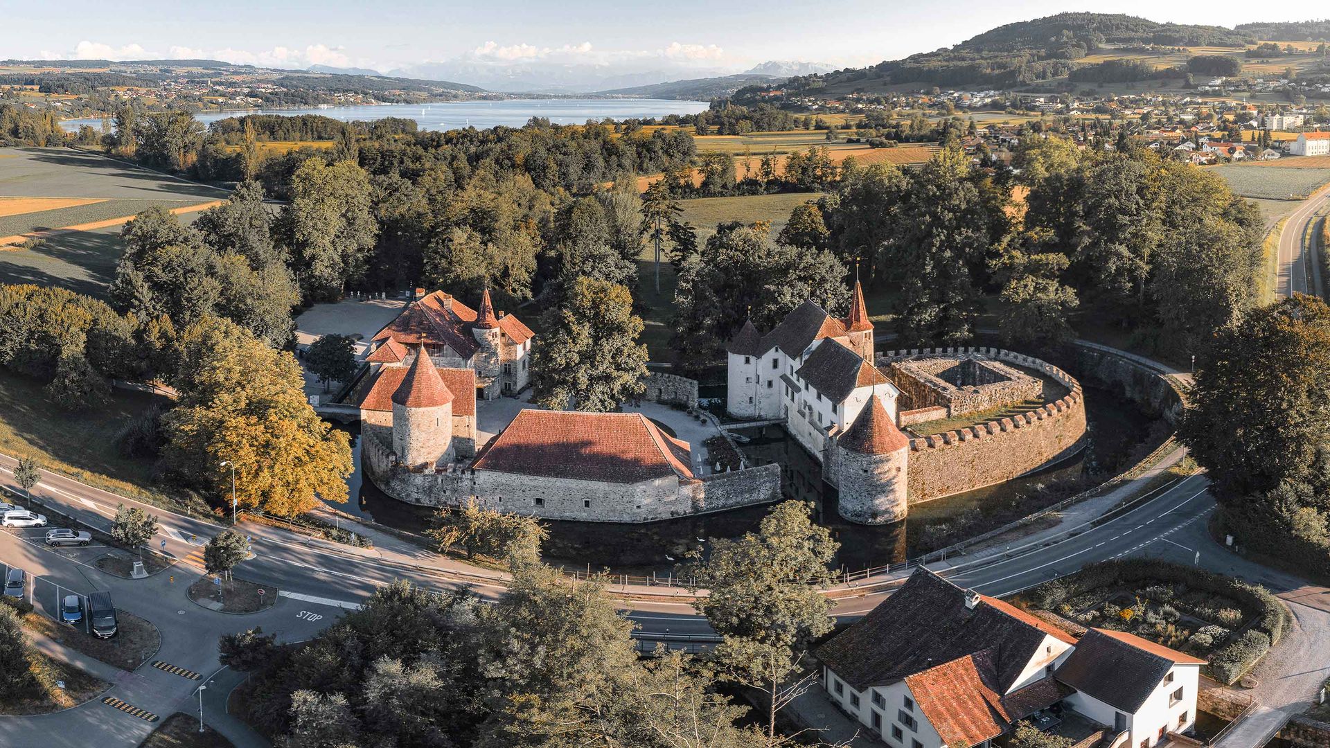 Veduta aerea di un maestoso castello circondato dal verde, con una strada tortuosa che lo raggiunge.