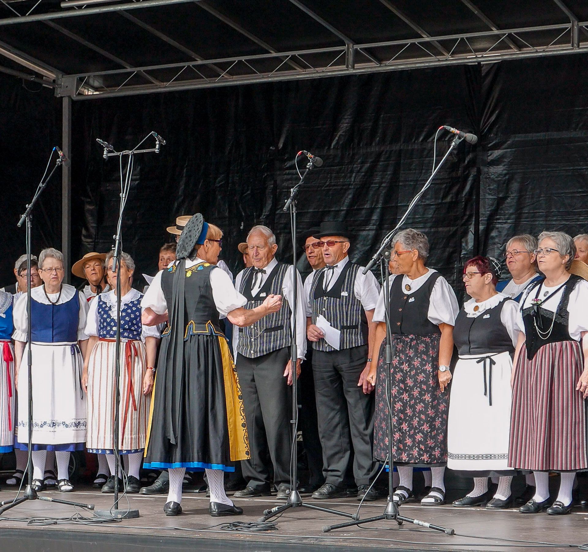 Gruppo di persone in costumi tradizionali su un palco con microfoni su supporti.