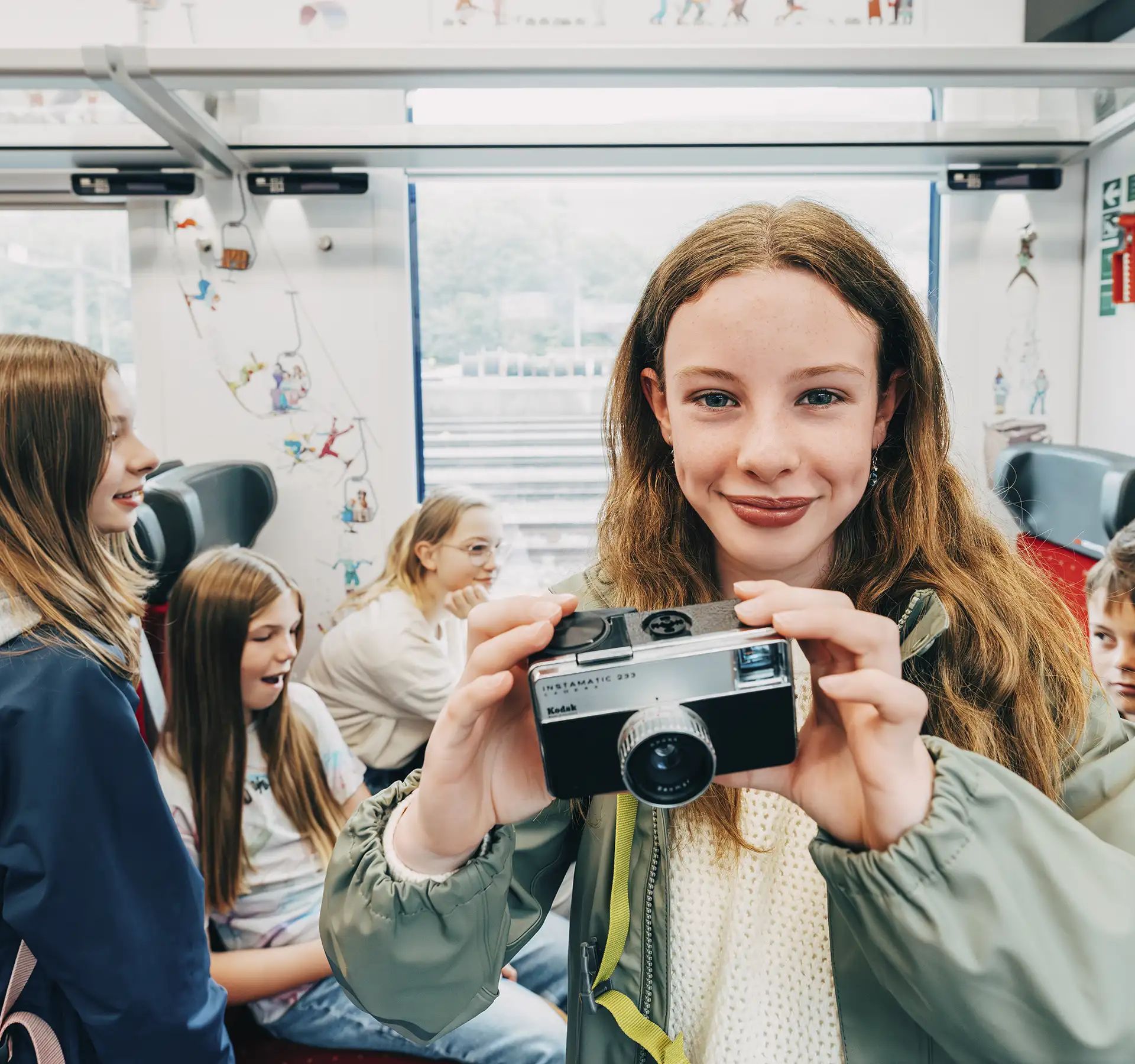 A girl stands in the train compartment and holds a camera into the picture.