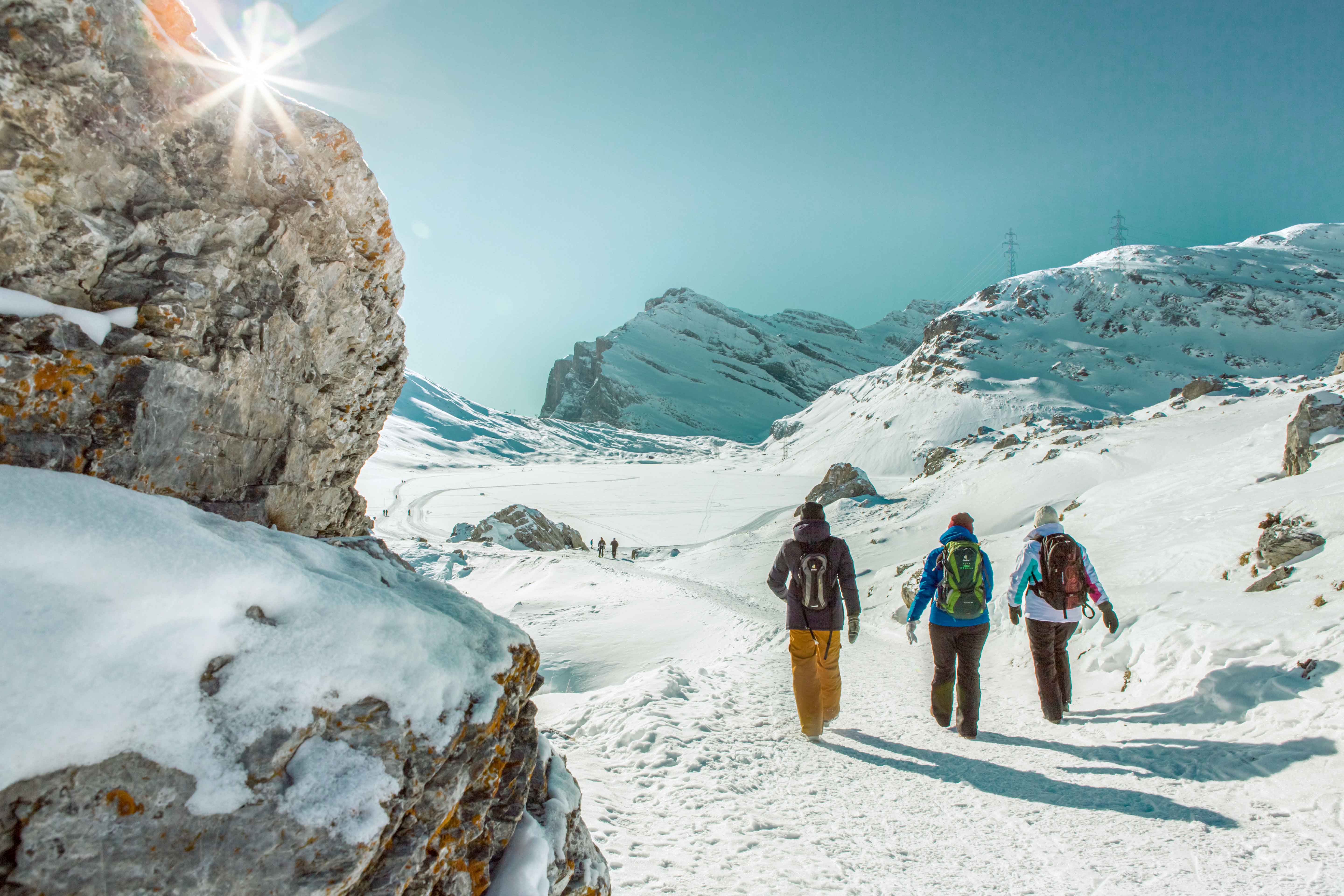 Tre individui che attraversano un sentiero di montagna innevato, circondati da un sereno paesaggio invernale.