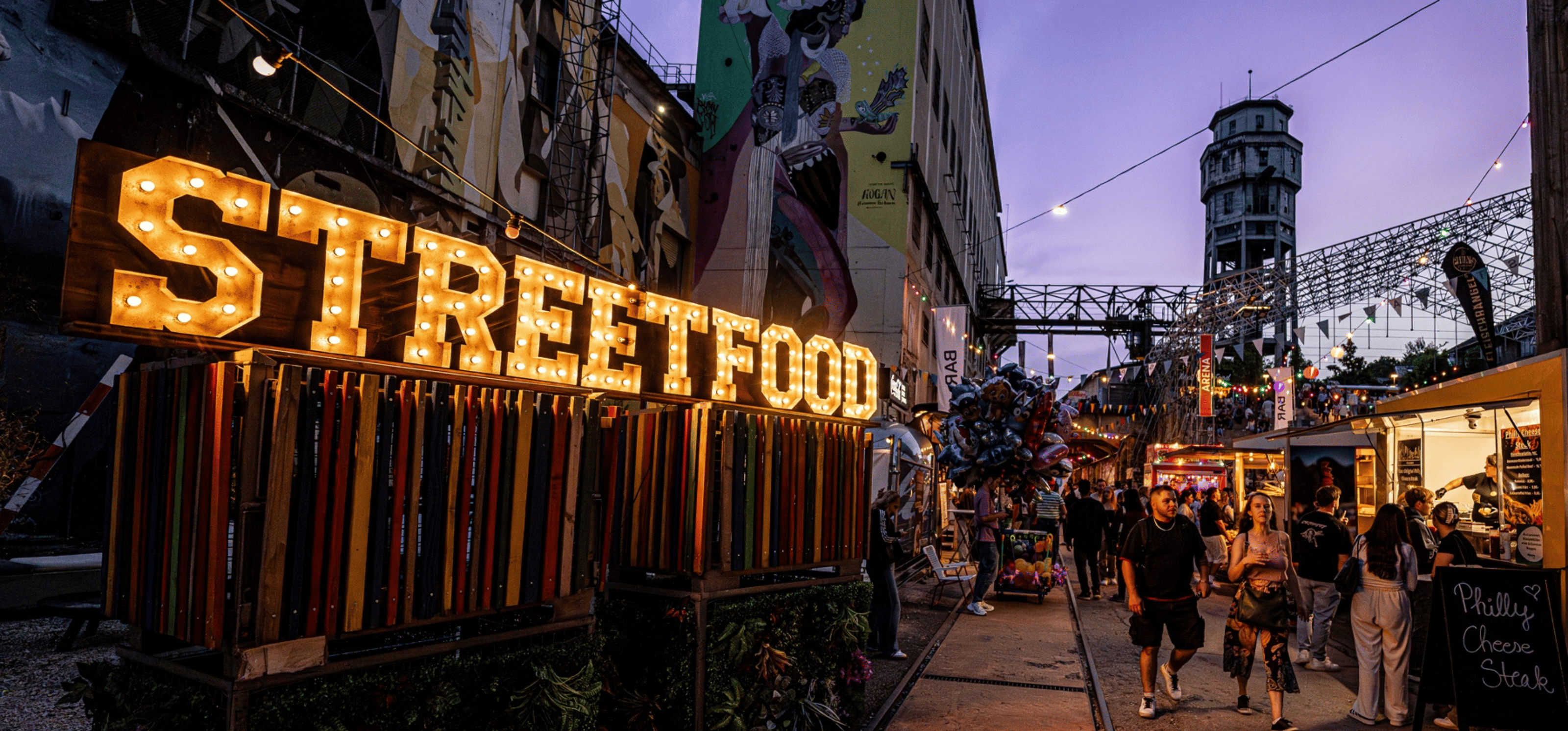 Des visiteurs se promènent dans un festival de street food avec des food trucks colorés, des guirlandes lumineuses et des stands de cuisine du monde entier.