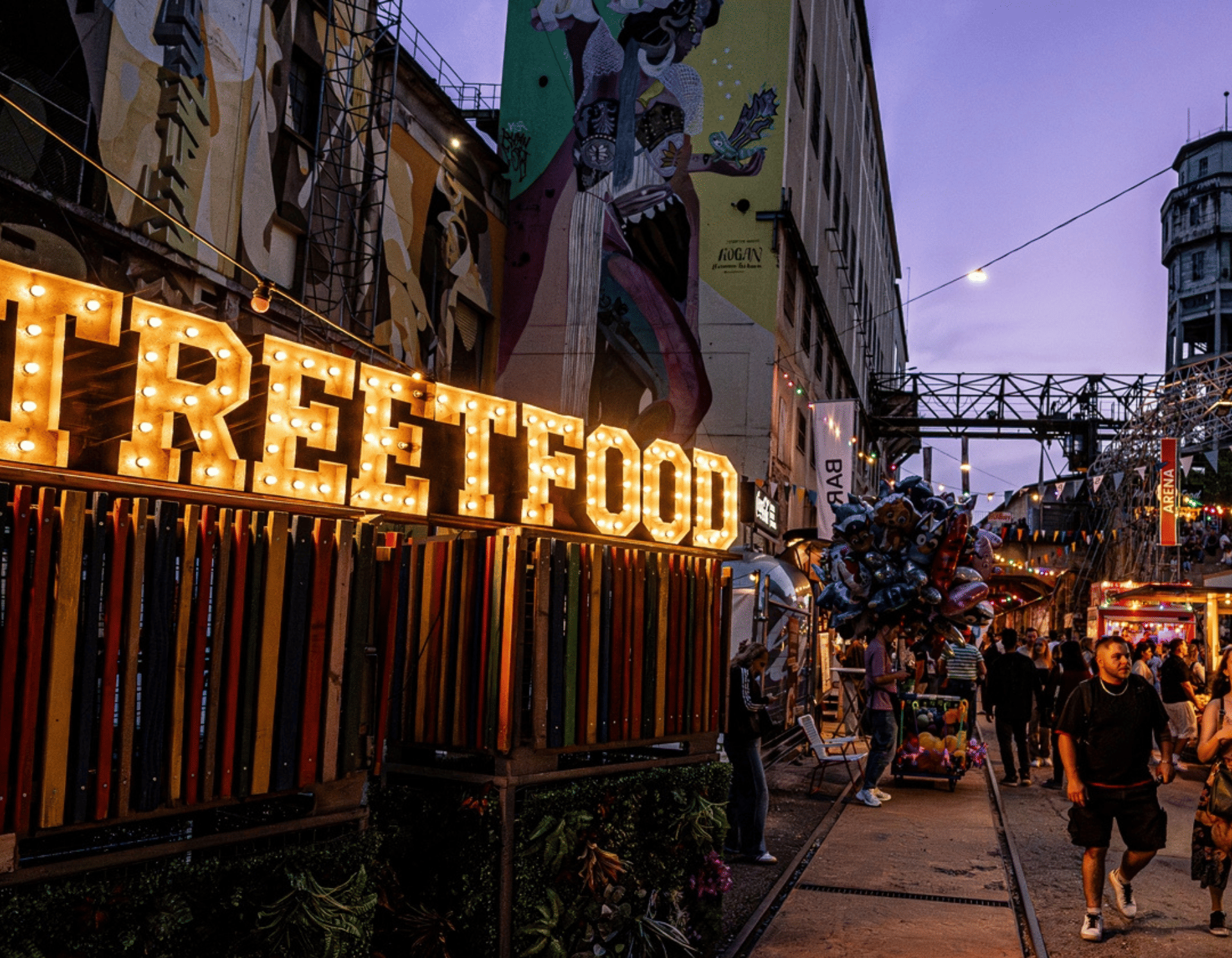 Visitors stroll through a street food festival with colorful food trucks, string lights, and food stalls from around the world.