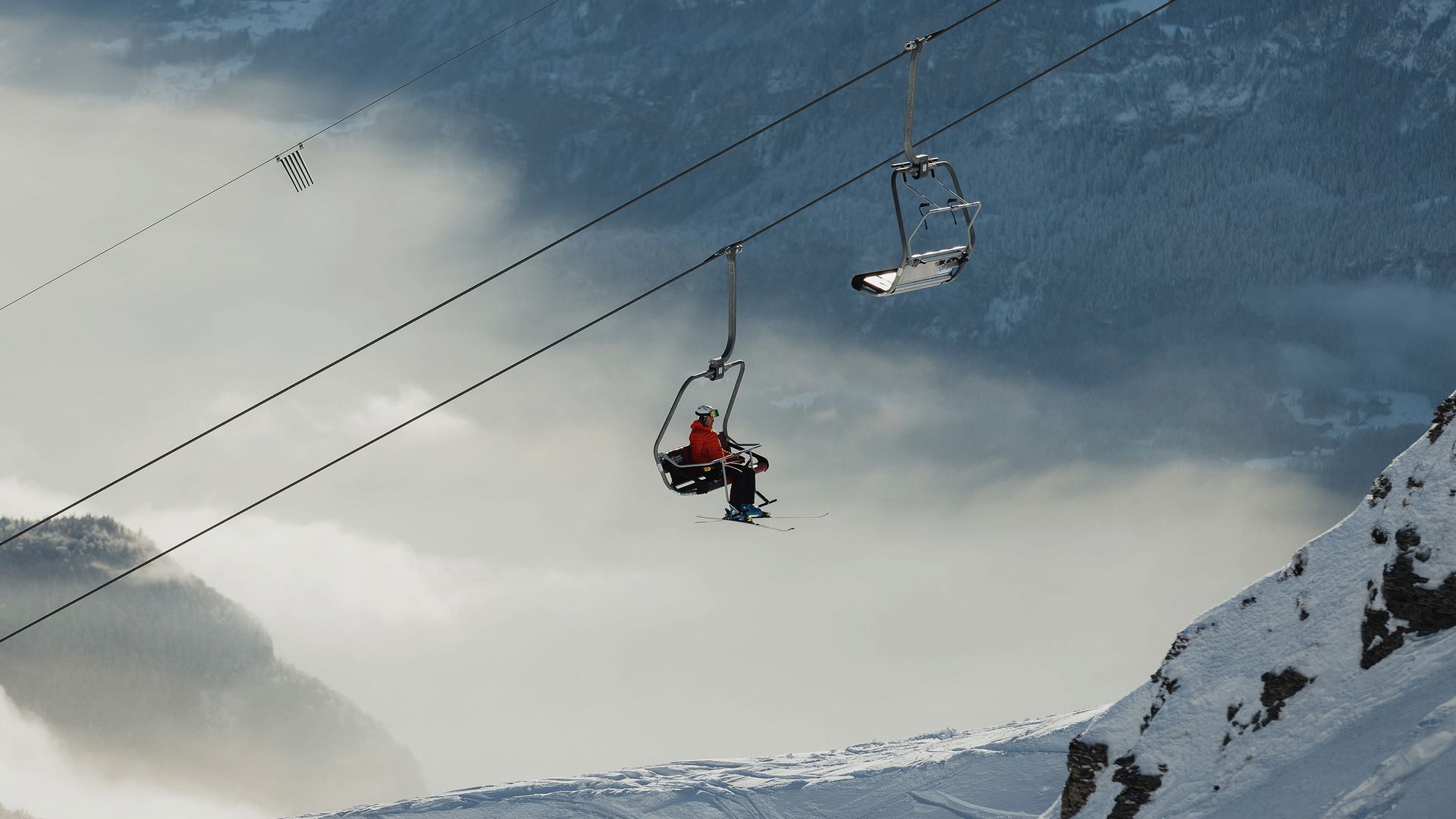 Chairlift in Sörenberg ski area with two people, one wearing a red jacket, above snowy mountain and clouds.