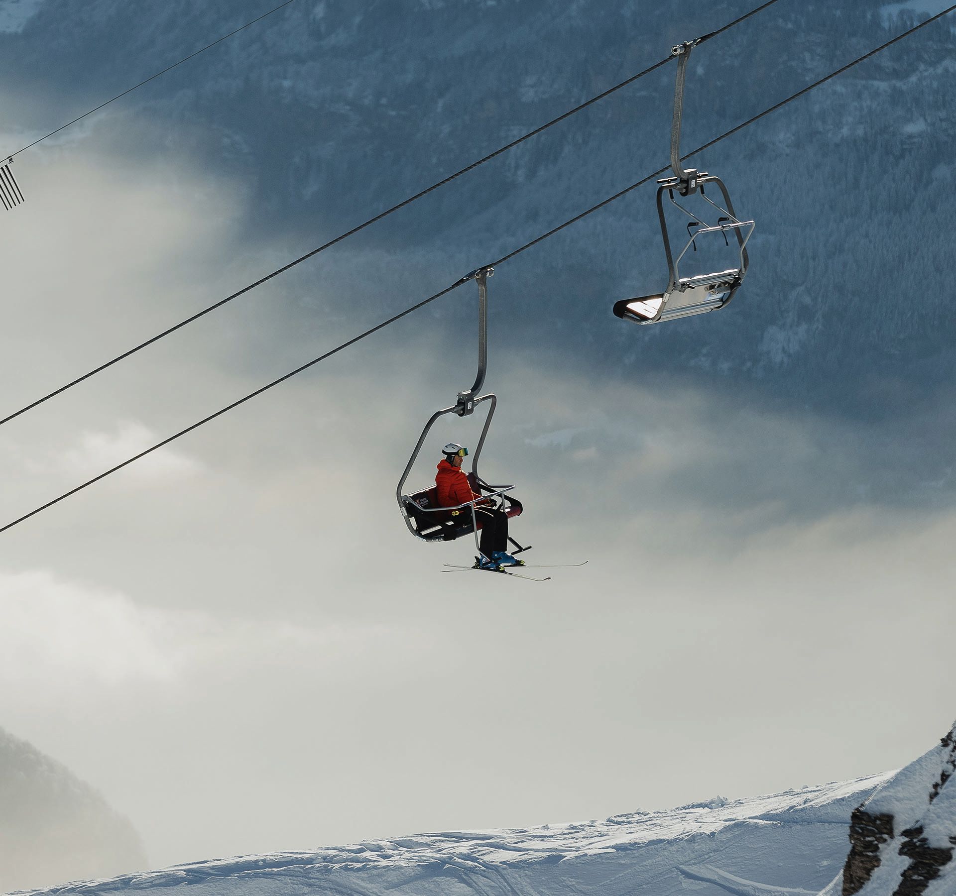 Sessellift im Skigebiet Sörenberg mit zwei Personen, eine trägt rote Jacke, über schneebedecktem Berg und Wolken.