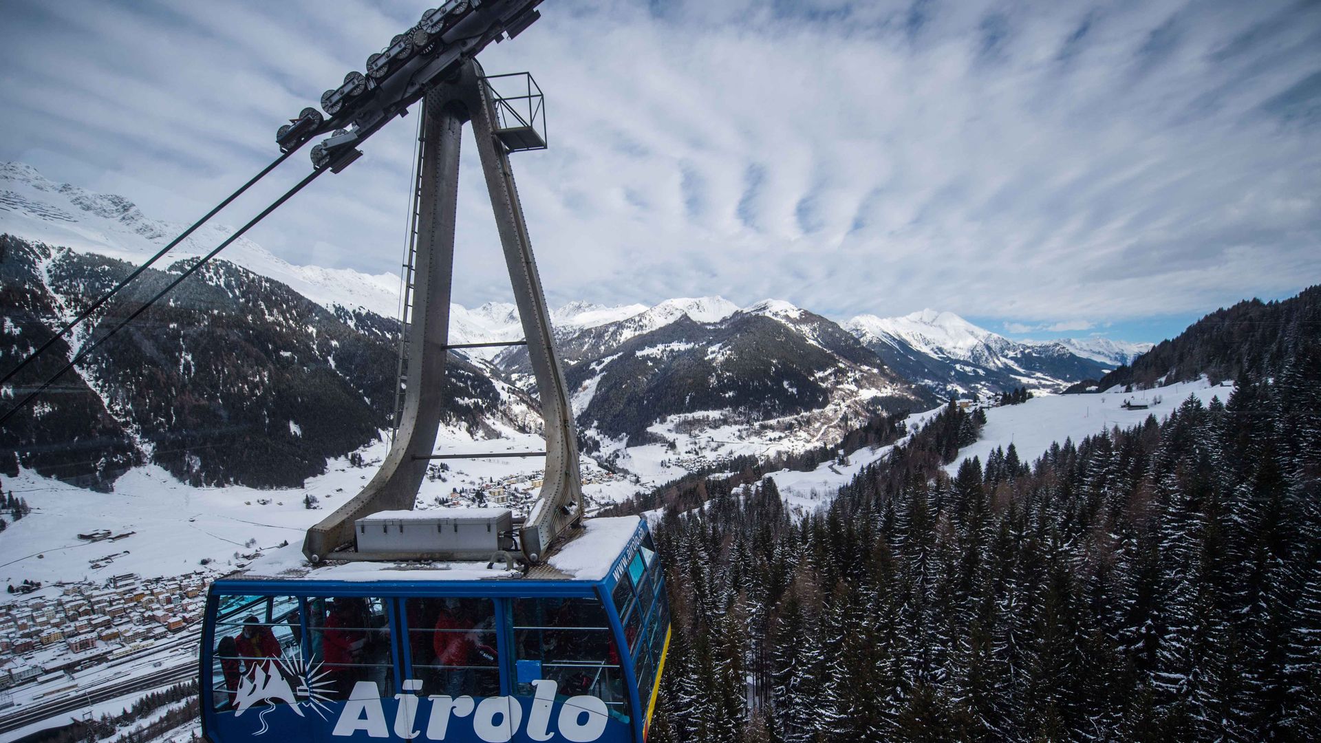 Una funivia scivola tra alberi innevati in un sereno paesaggio montano.