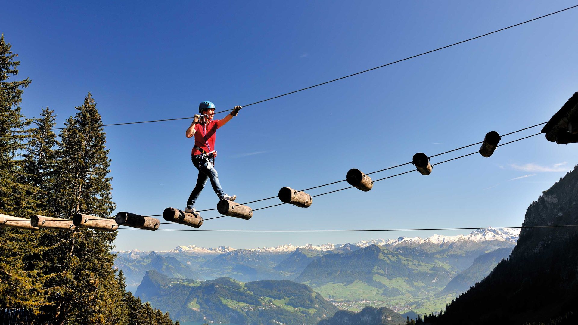 A person carefully walking on a rope bridge high above a stunning mountain landscape.