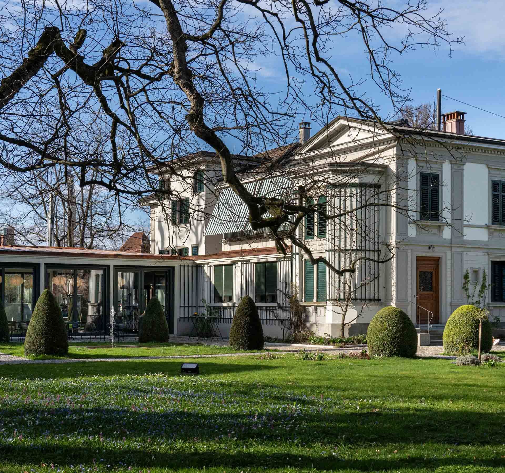 Un'antica villa con un giardino verde e un albero di fronte