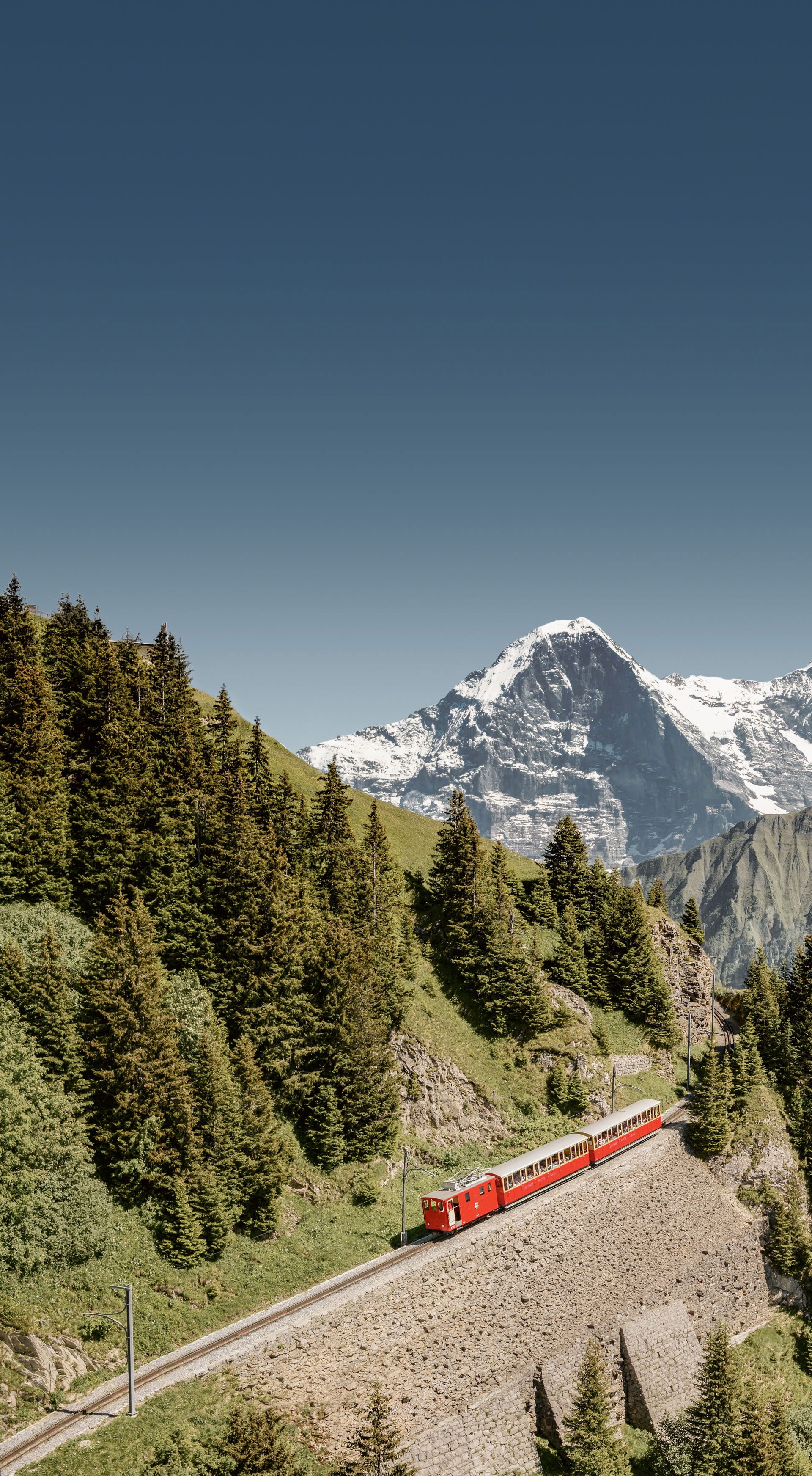 Luftaufnahme der Zahnrad welche den Berg hinochfährt. Im Hintergrund sind verschneite Berggipfel Eiger, Mönch und Jungfrau zu sehen.