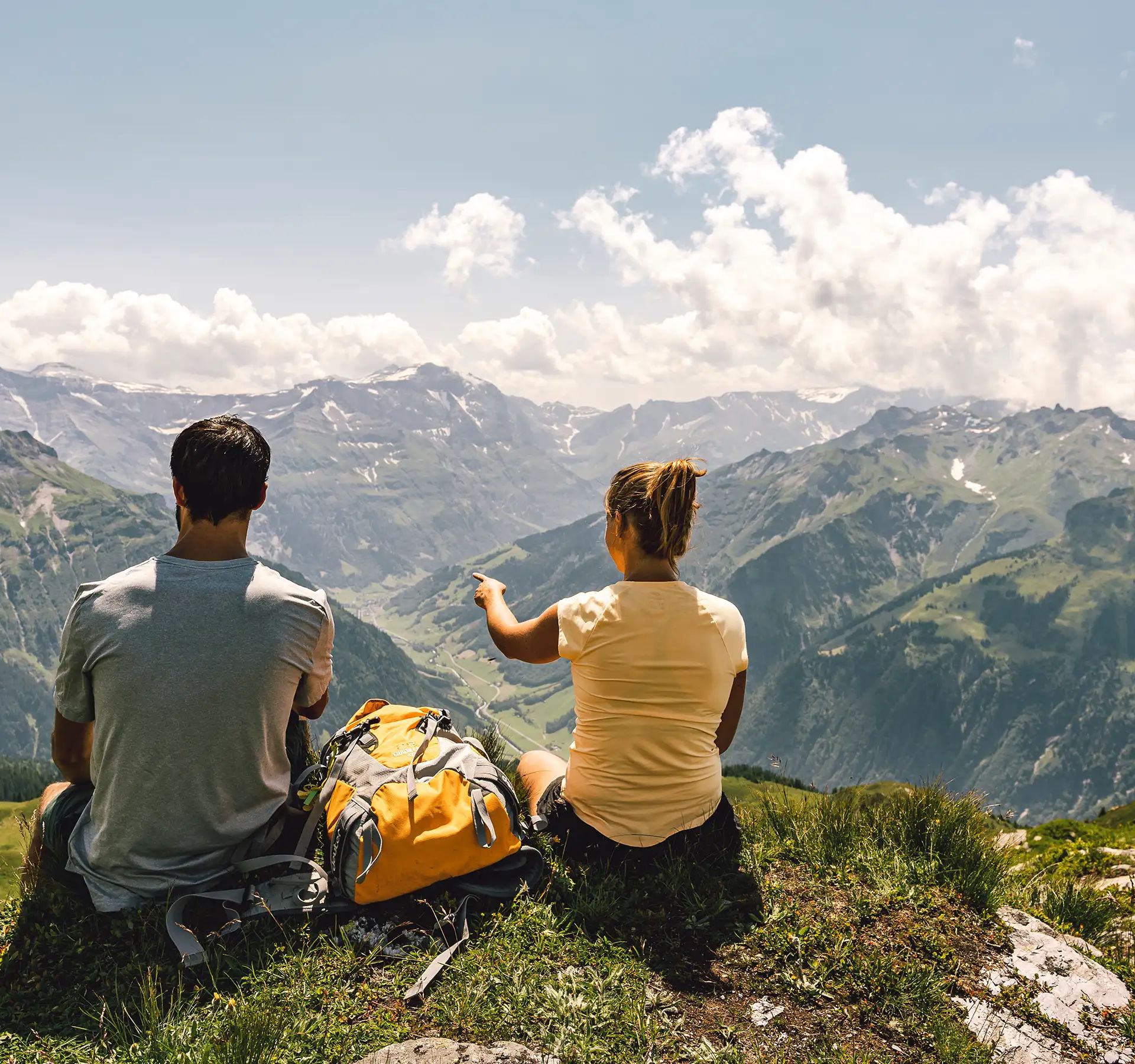 Due persone sono sedute a terra e si godono insieme una splendida vista sul mondo alpino.