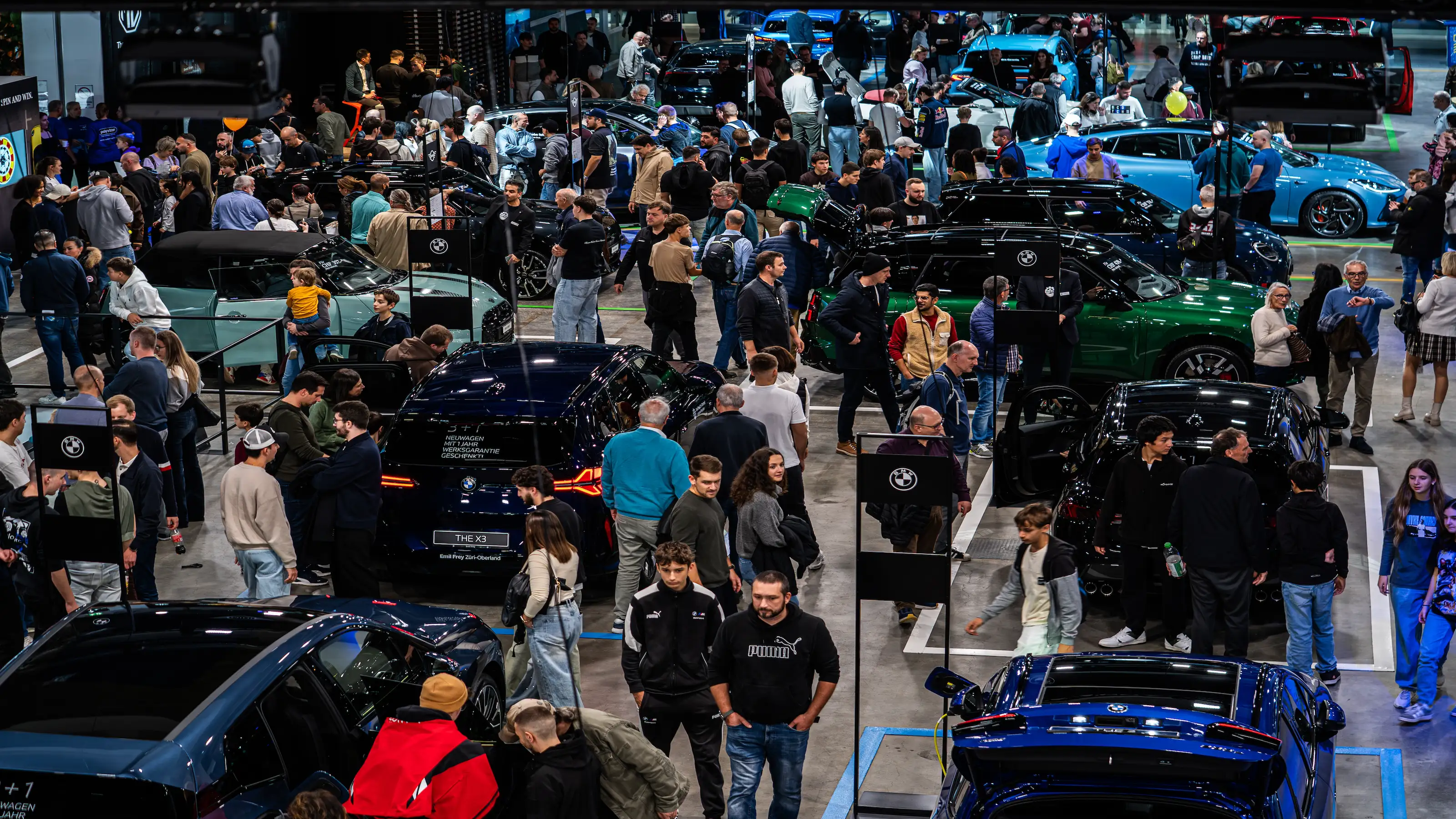 Foule de personnes lors d'un salon automobile avec plusieurs véhicules exposés dans un hall.