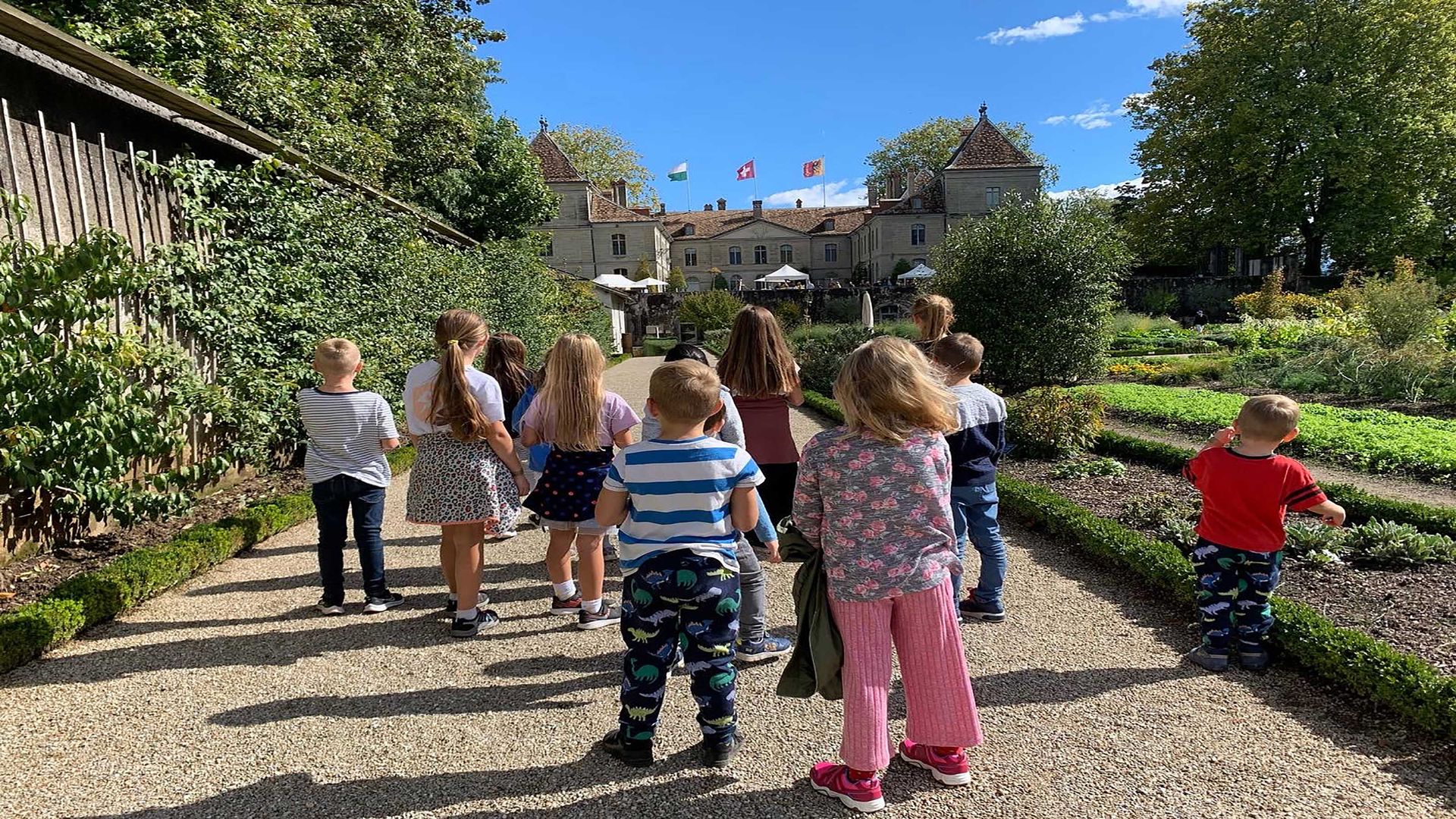 Un gruppo di bambini in un giardino che guardano il castello di Prangins con le bandiere sullo sfondo.