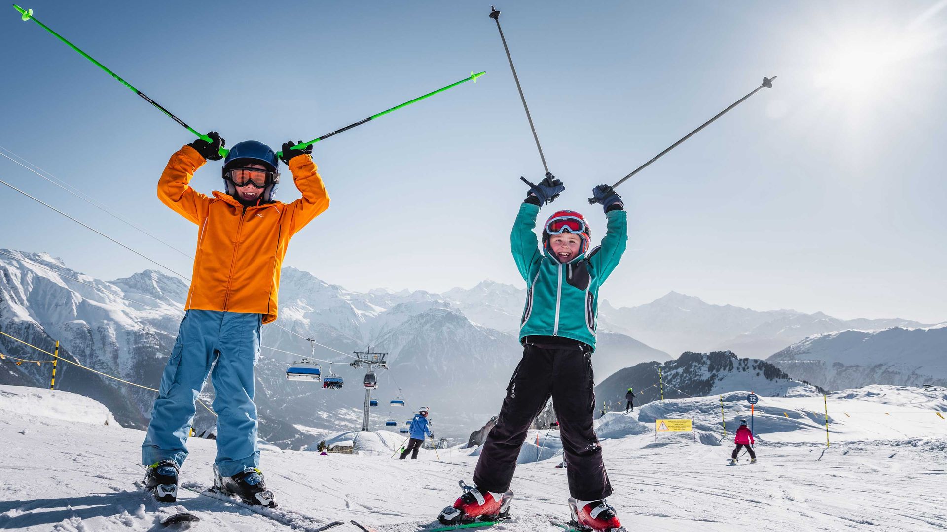 Zwei Kinder auf Skiern heben vor Freude ihre Arme in die Luft.