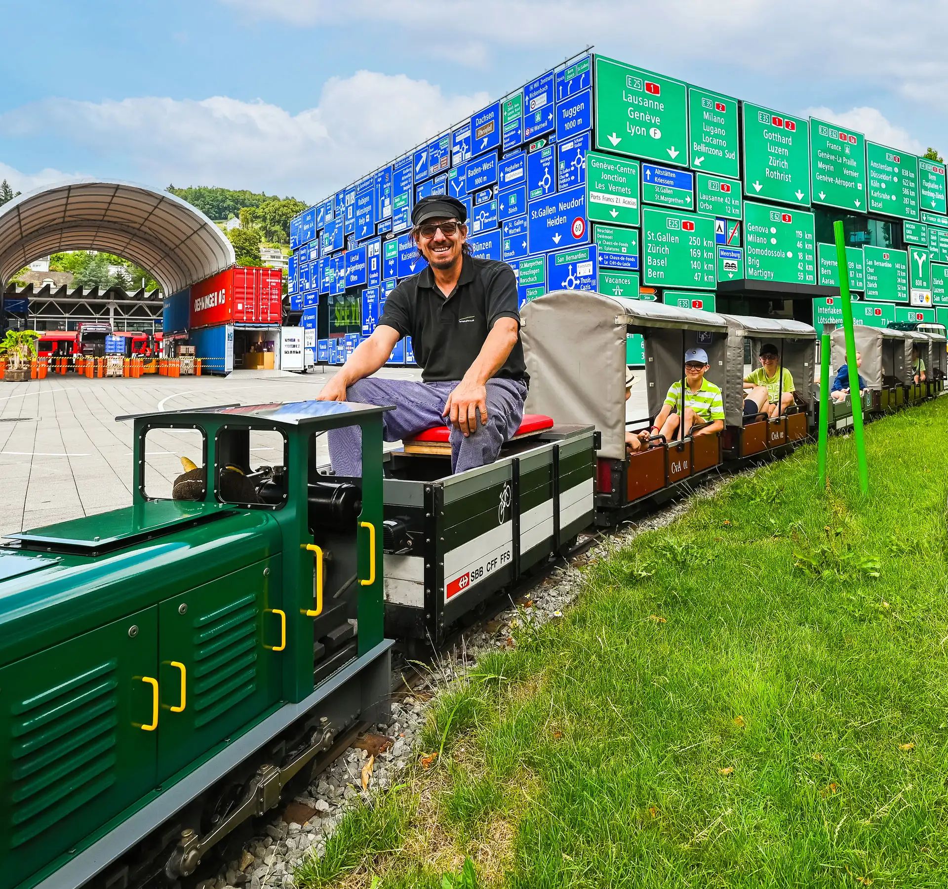 Un modellino ferroviario in miniatura con un treno verde e diverse carrozze aperte, occupato da bambini, sui binari del Museo Svizzero dei Trasporti.