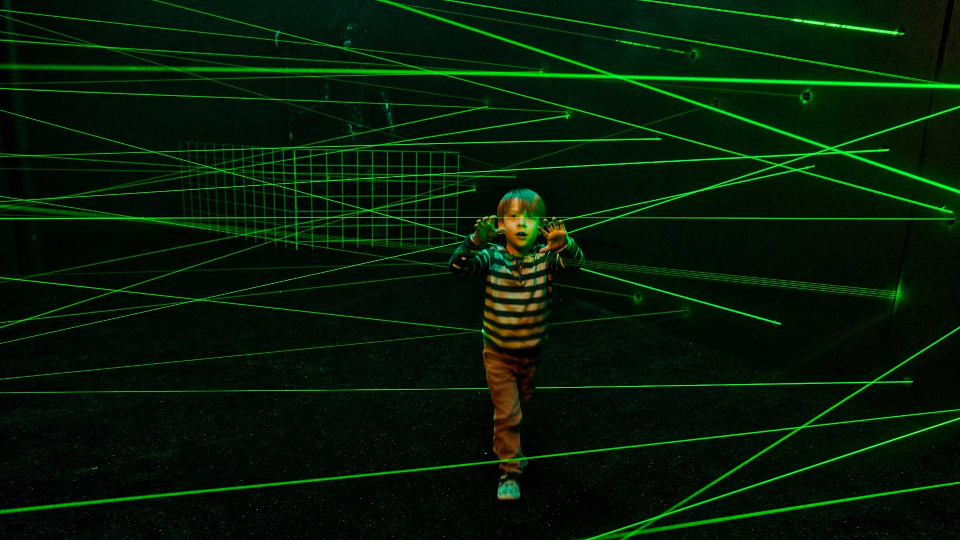 Un ragazzo si trova affascinato in una stanza buia con molti laser verdi.