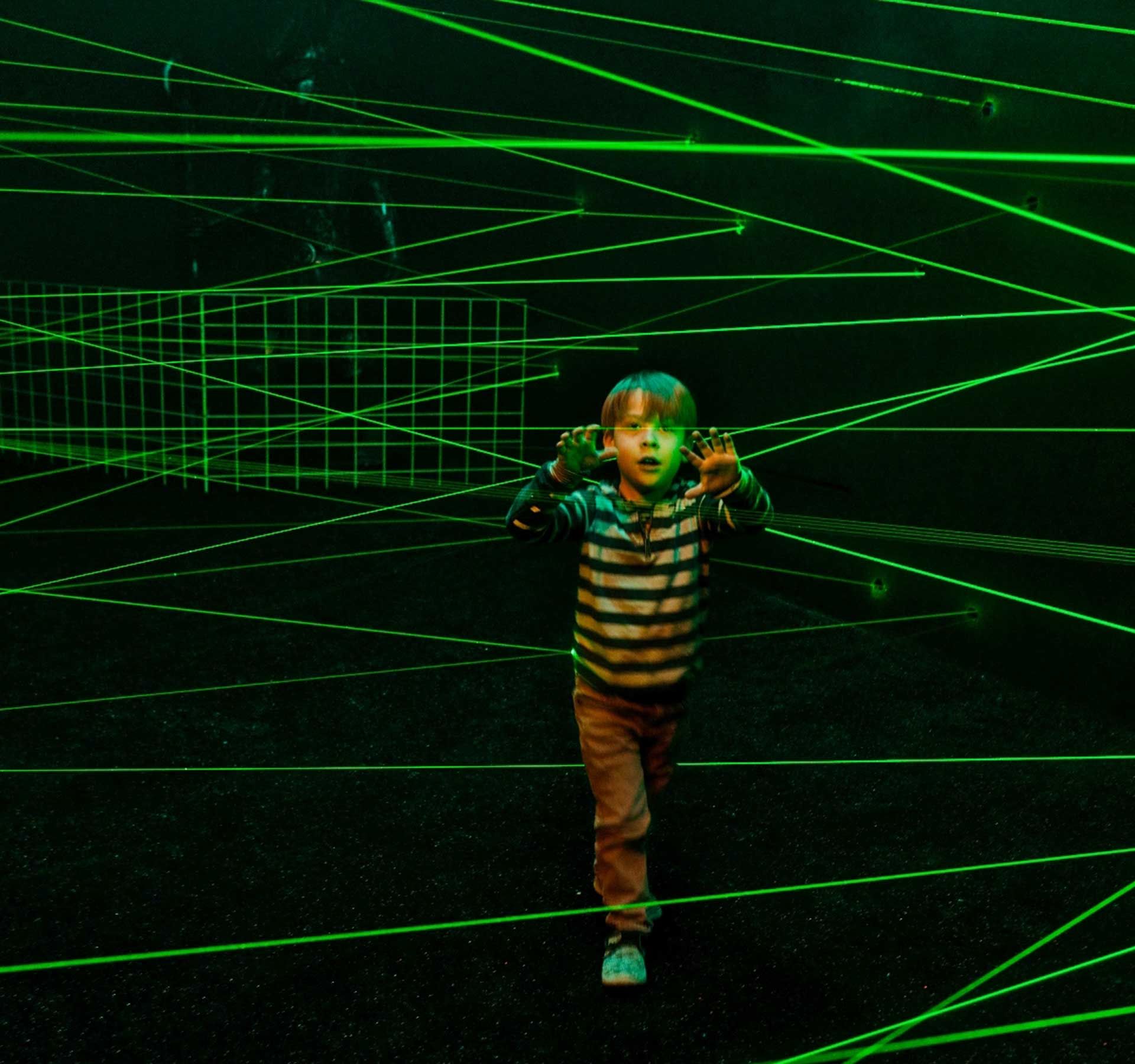 A young boy stands fascinated in a dark room with lots of green lasers.