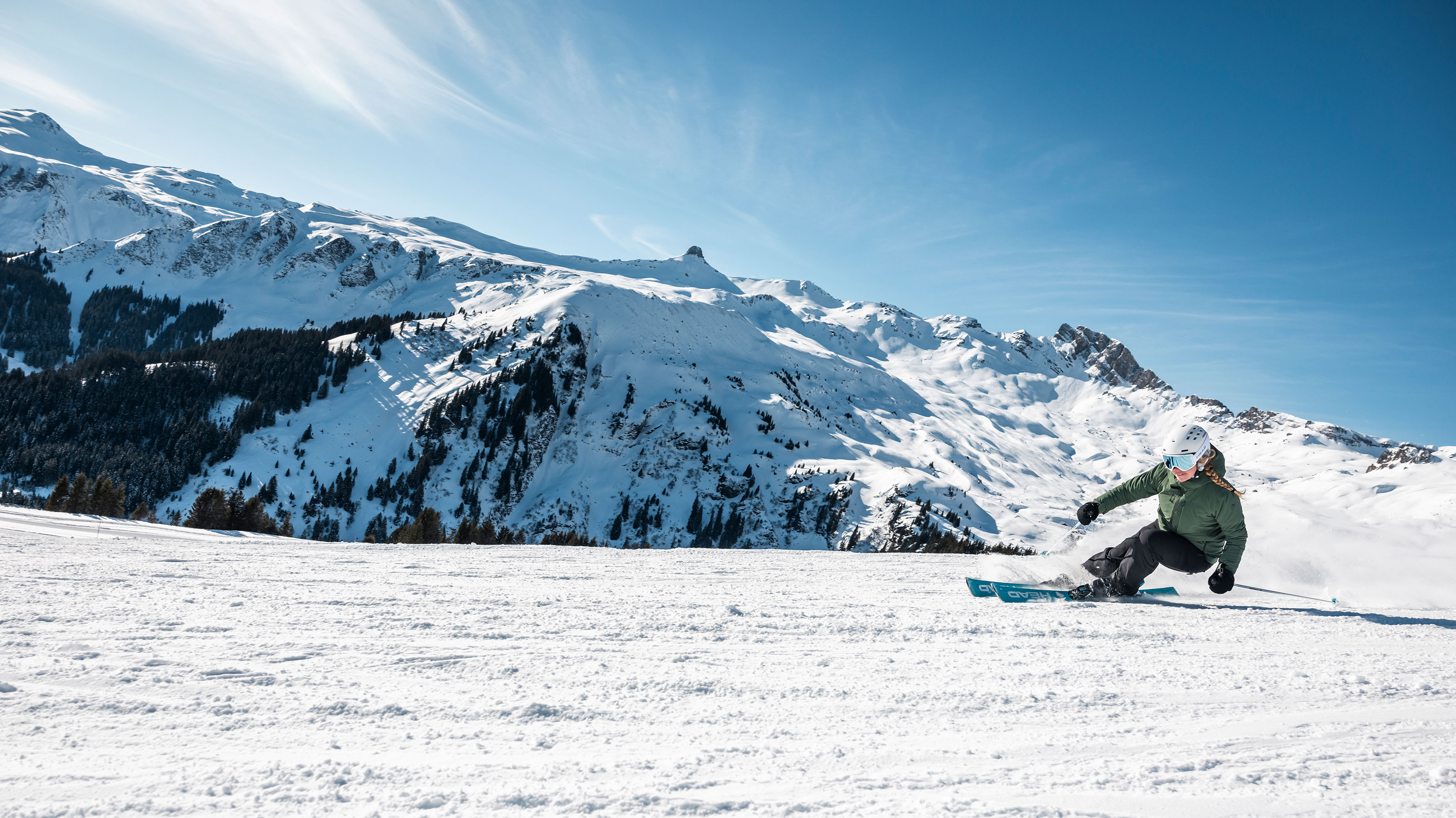 Une skieuse descend la piste, avec en arrière-plan un magnifique paysage montagneux.