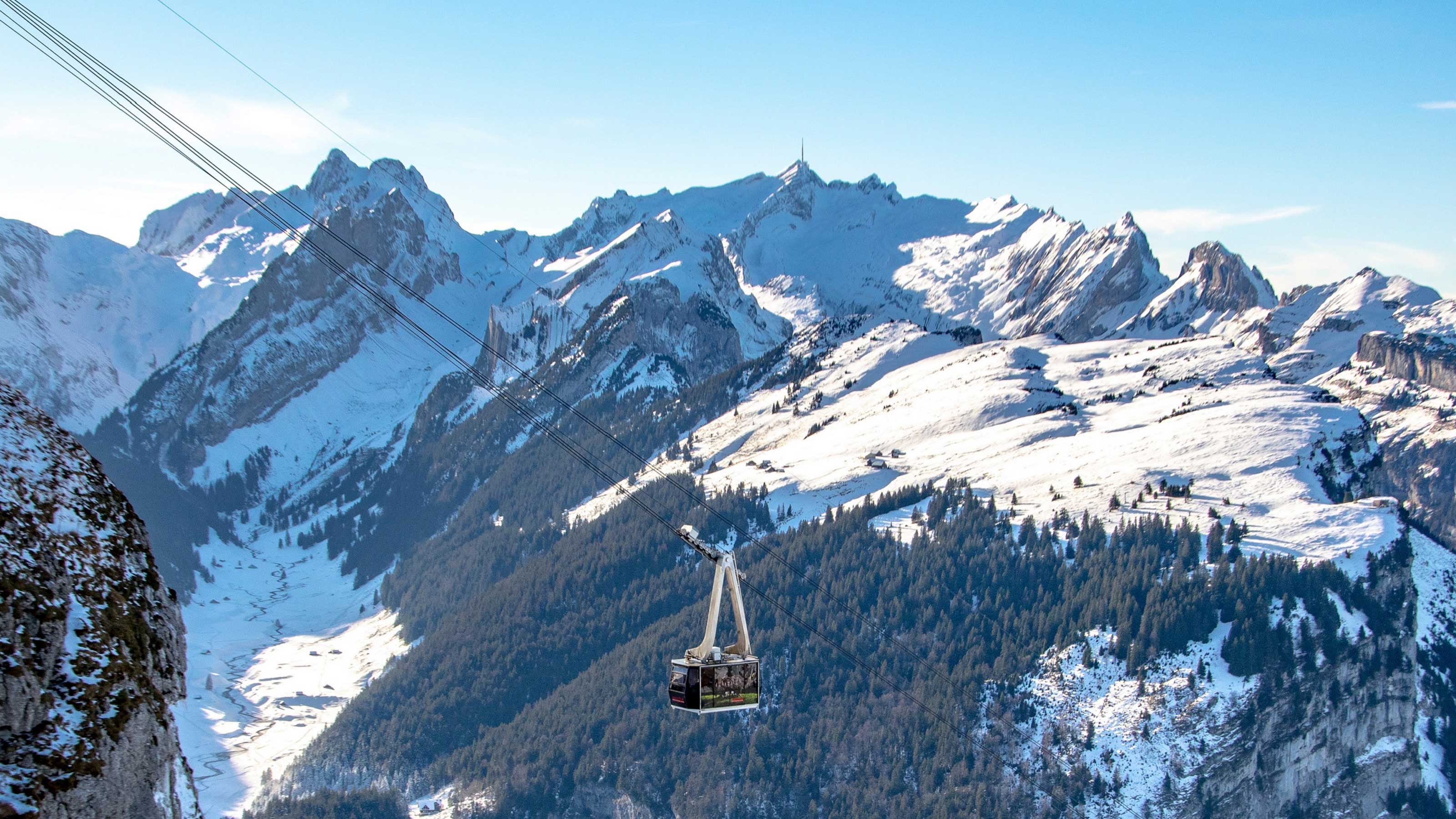 Una funivia sospesa in un paesaggio montano innevato sullo sfondo.
