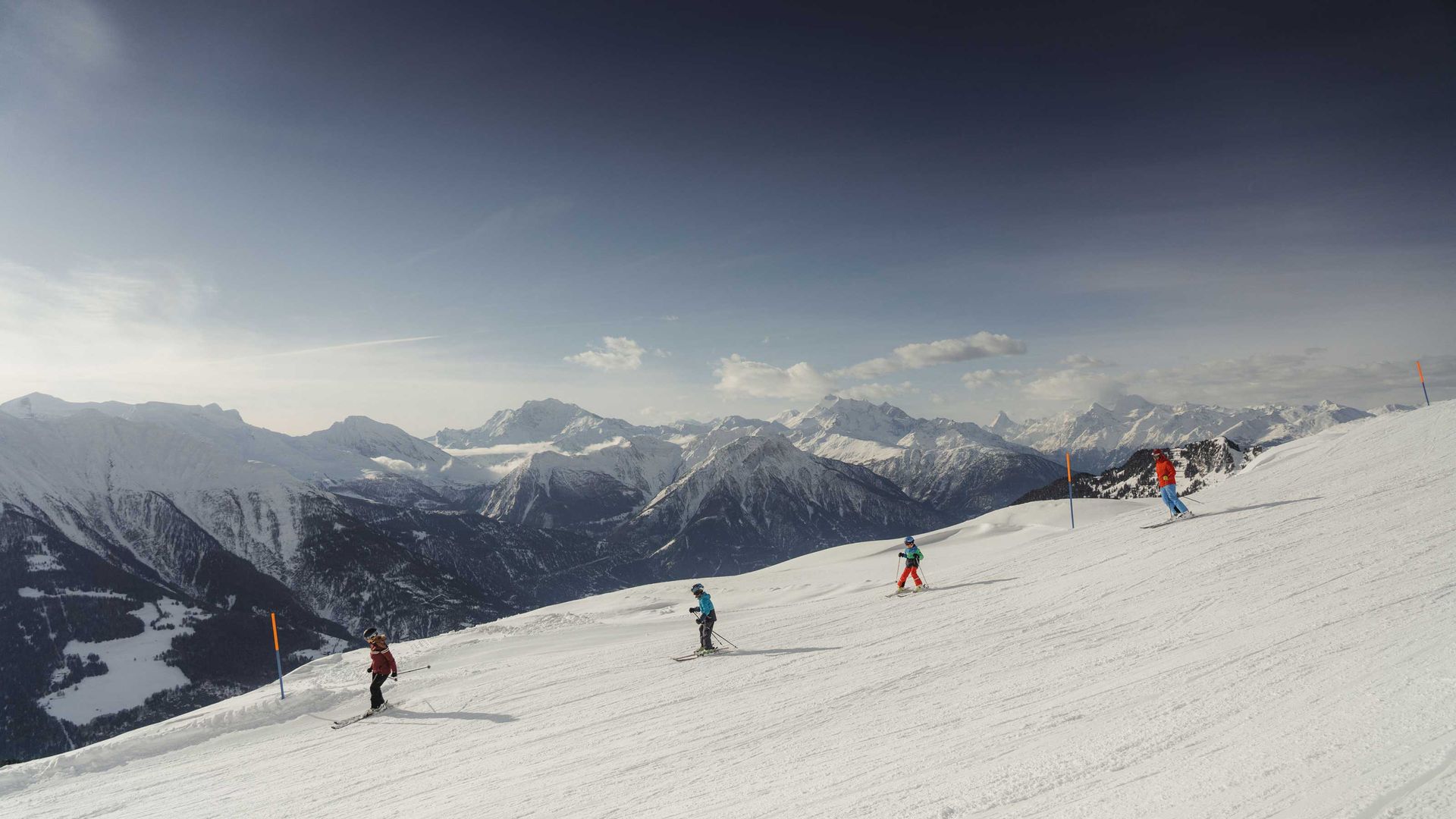 A family skiing on perfectly groomed pistes under a bright blue sky
