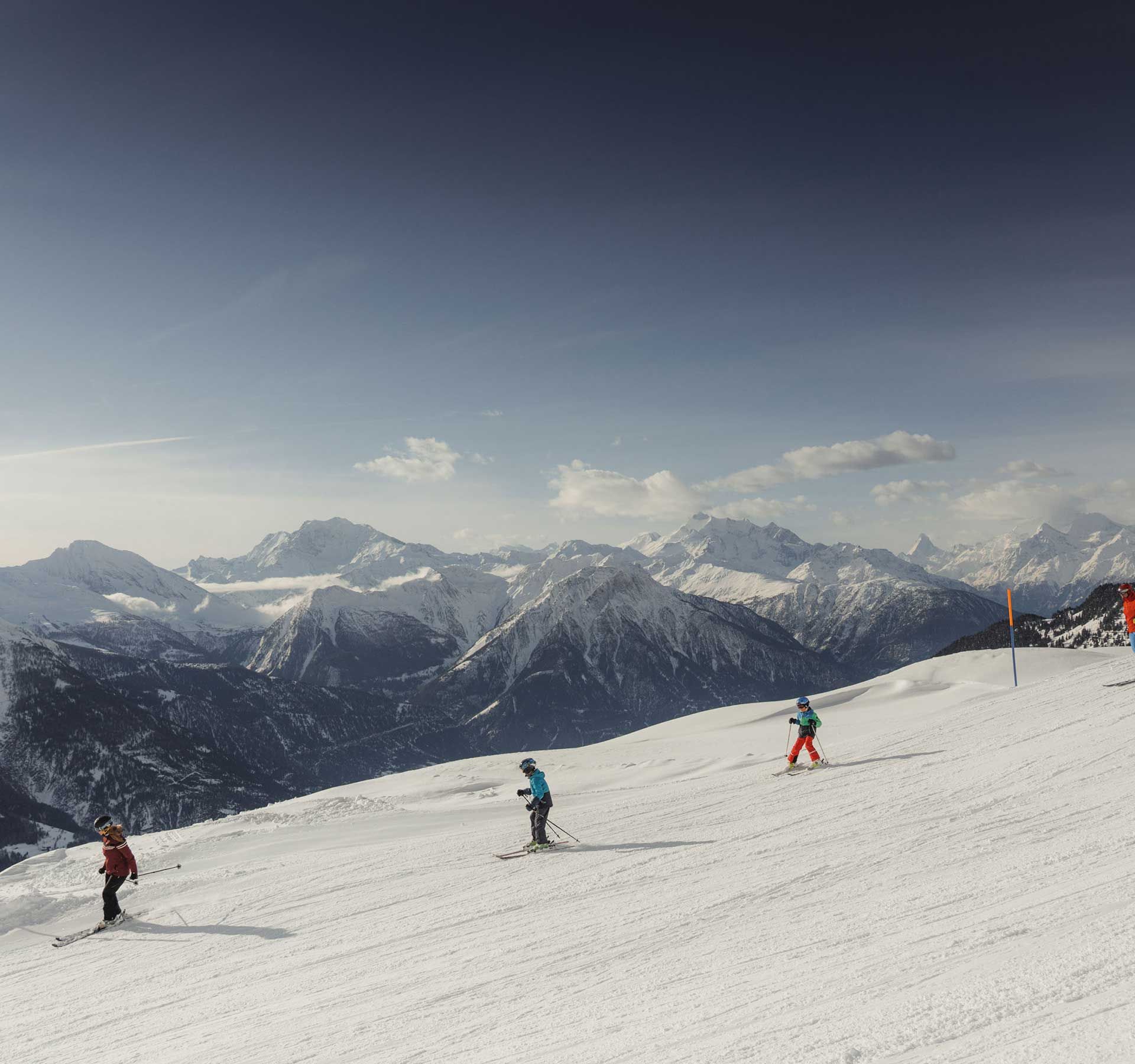 Une famille en train de skier sur des pistes parfaitement préparées et sous un ciel bleu éclatant
