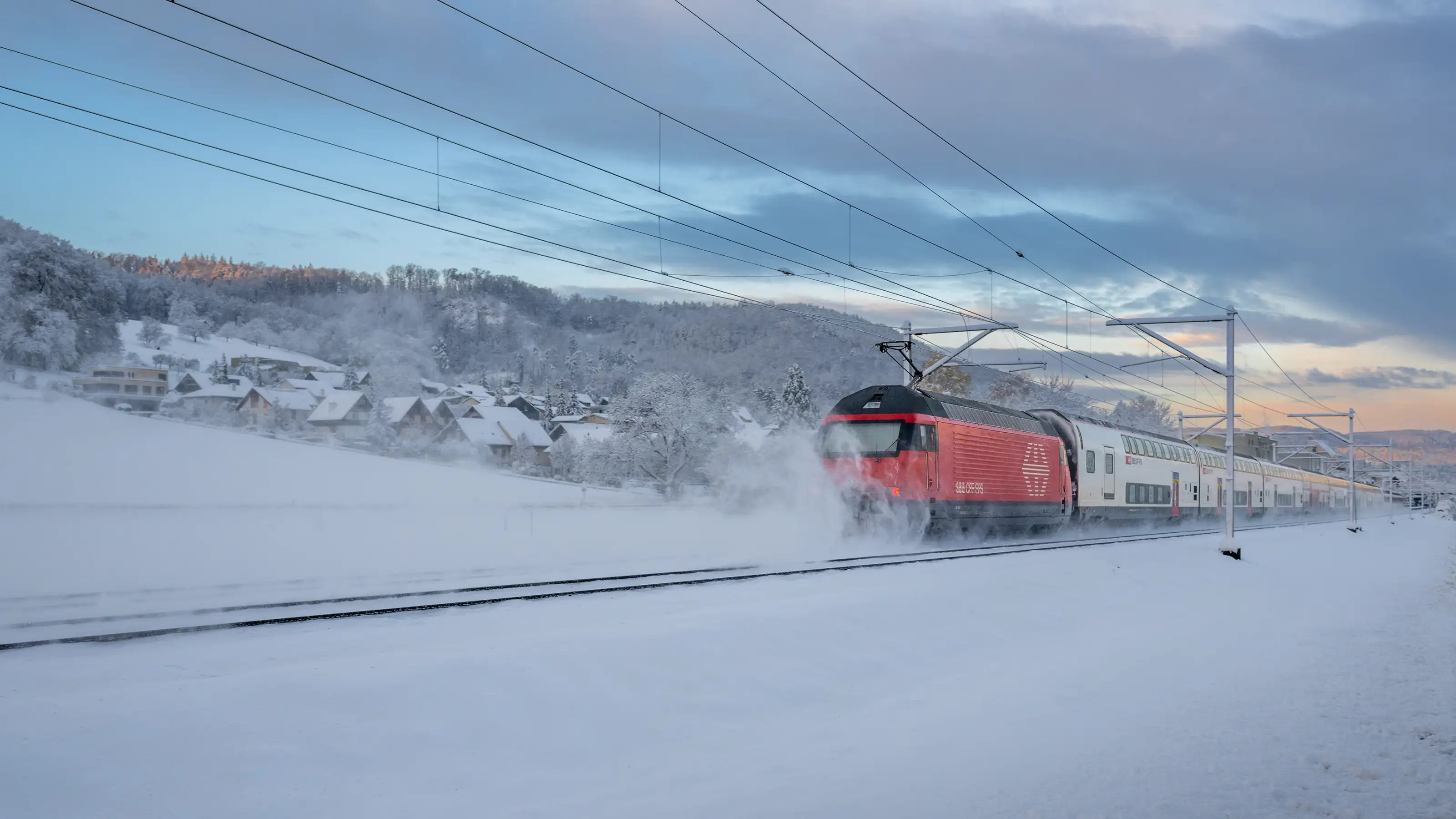 Un treno delle FFS percorre una linea ferroviaria innevata attraverso un paesaggio montano invernale.