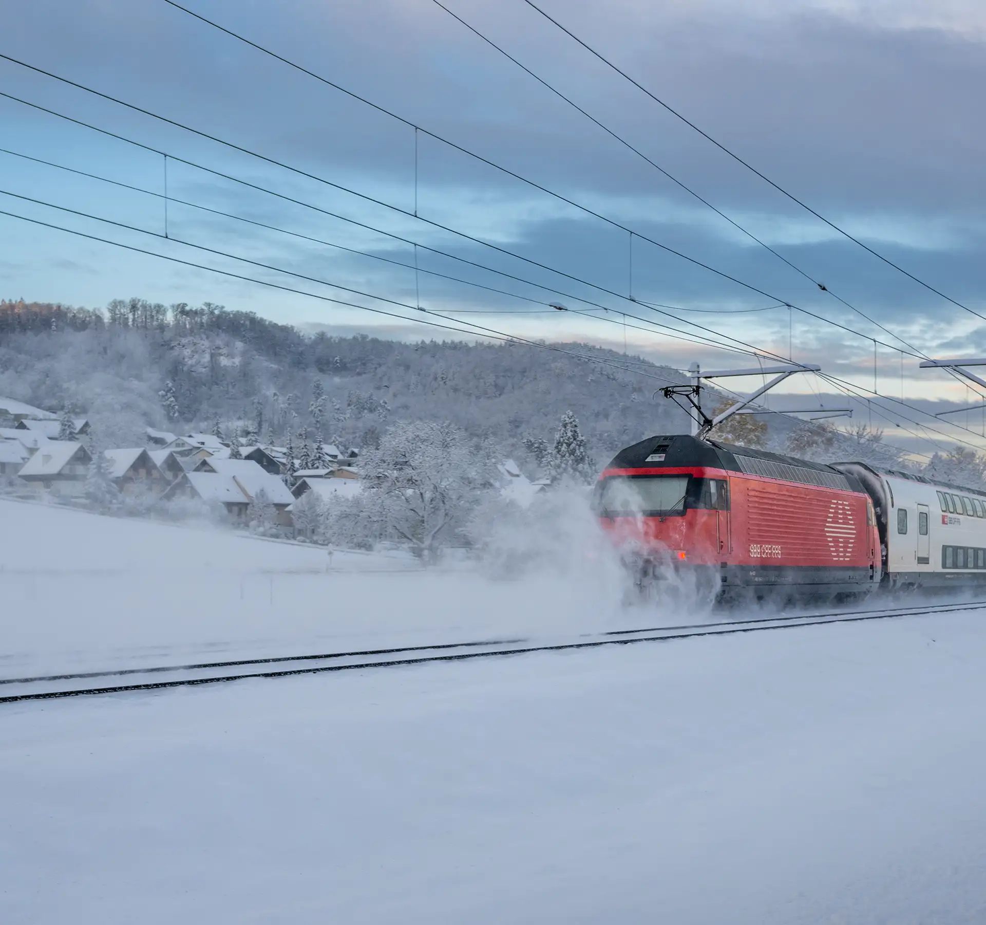 Un treno delle FFS percorre una linea ferroviaria innevata attraverso un paesaggio montano invernale.