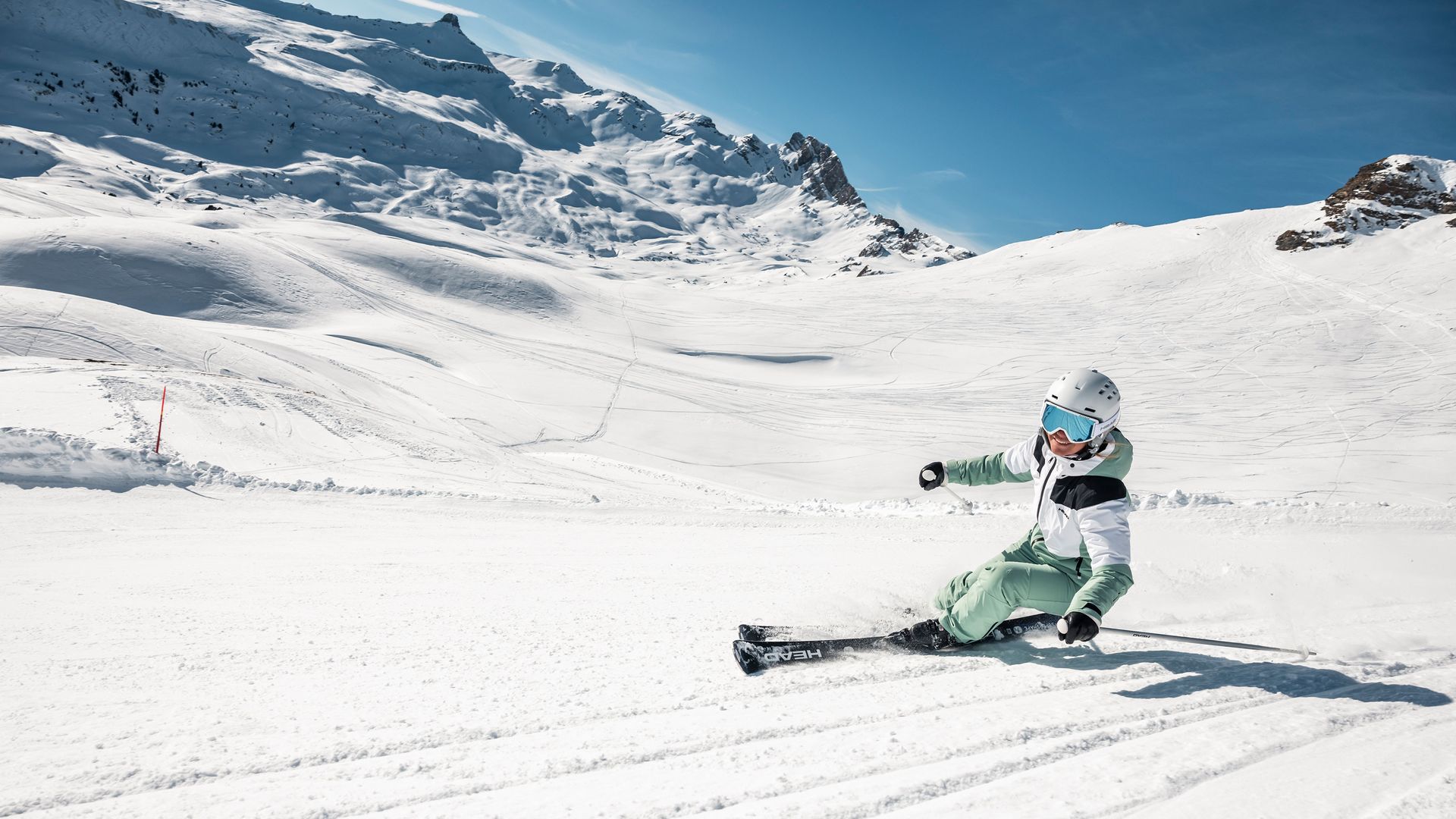 Das Bild zeigt eine gruppen von Skifahrern, die bei herrlichem, sonnigen Winter eine Piste hinunterfahren.