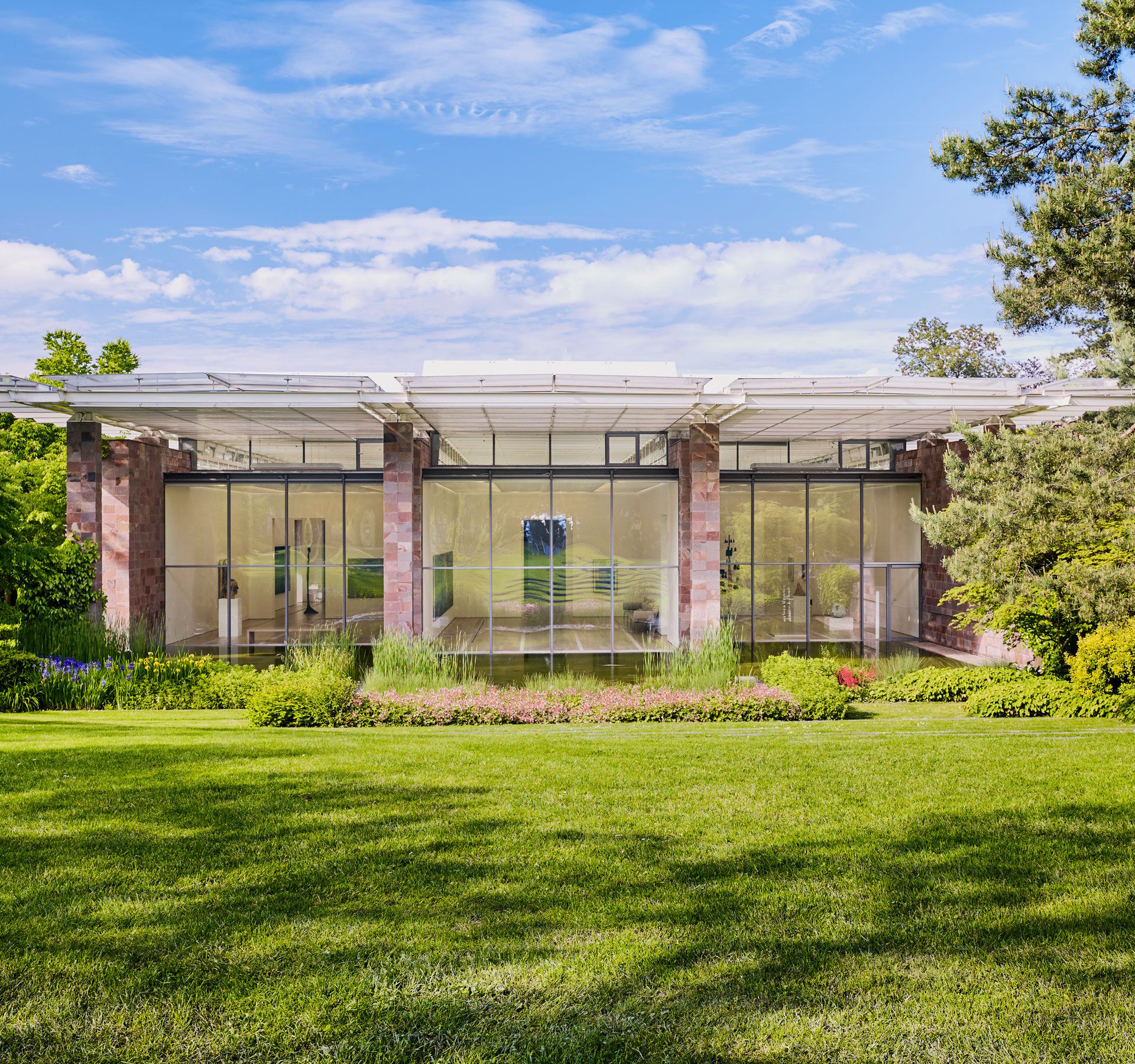 Modern architecture, surrounded by a well-tended garden and large trees under a blue sky
