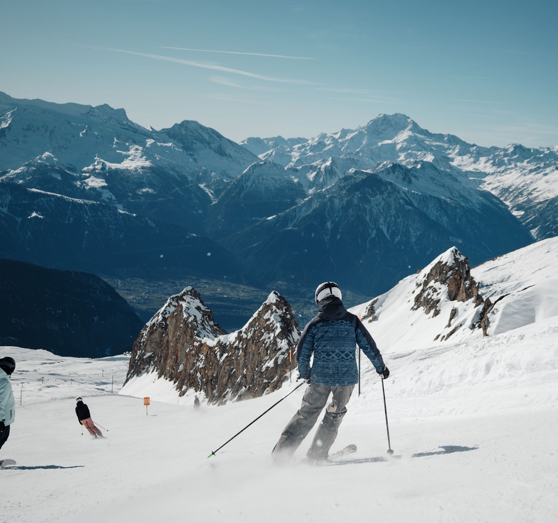 Più sciatori scendono una pista innevata nell'area sciistica di Blatten Belalp con cime montuose sullo sfondo.