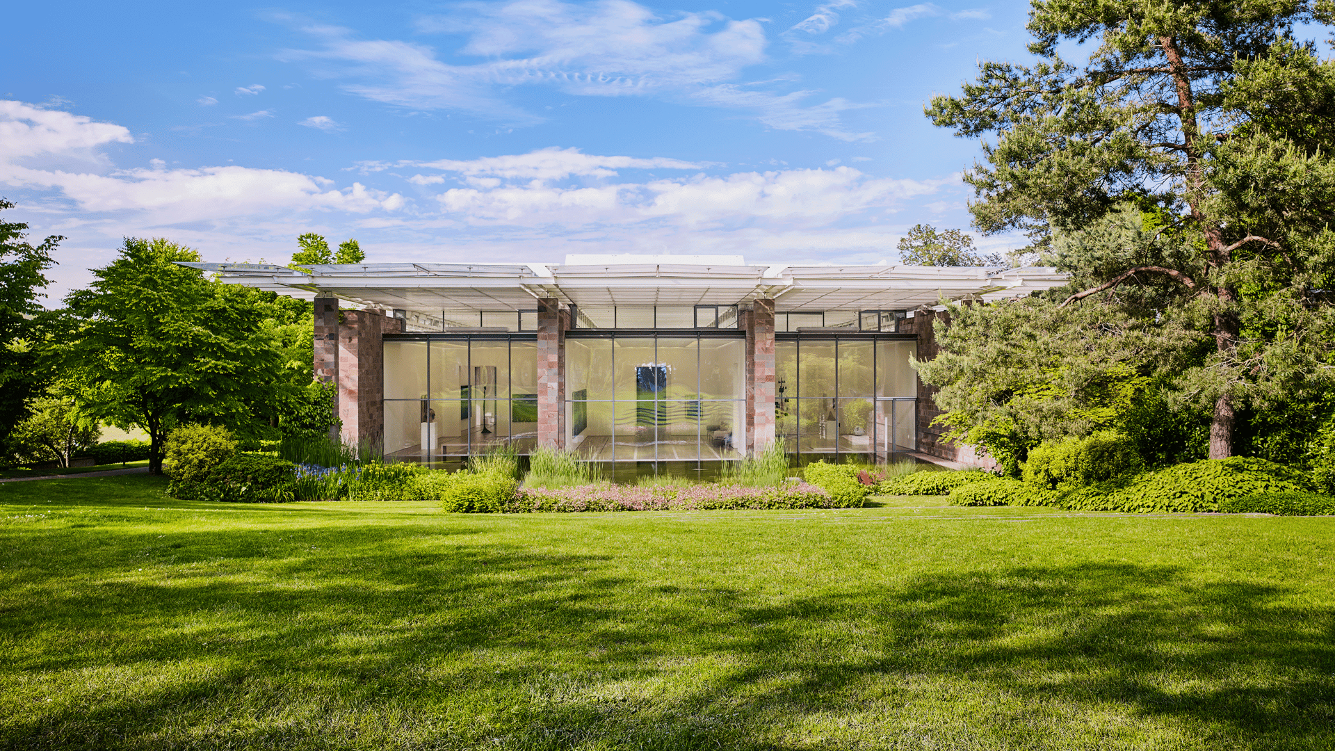 Modern architecture, surrounded by a well-tended garden and large trees under a blue sky