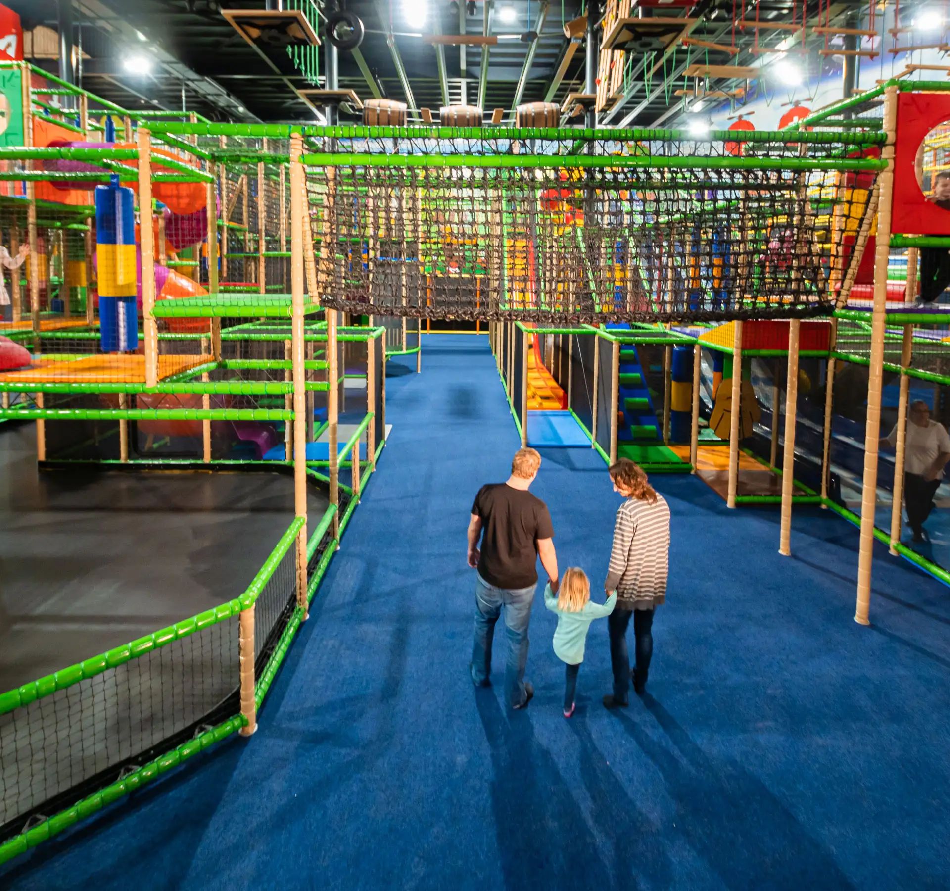 Blick in den Kiddy Dome mit buntem Klettergerüst und drei Personen, die auf blauem Boden darauf zugehen