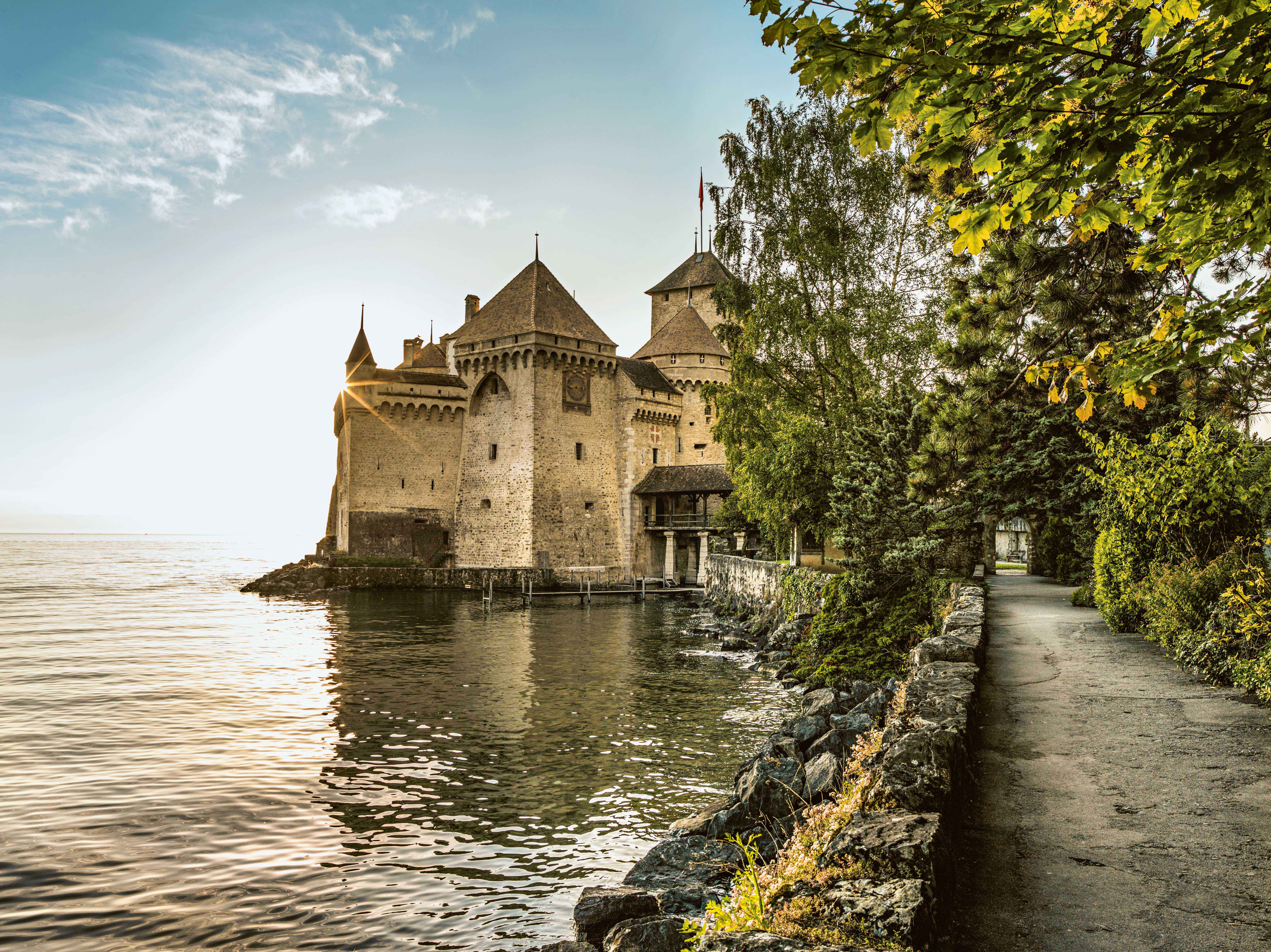 Ein Schloss steht malerisch am Ufer eines Sees, umgeben von einer idyllischen Landschaft.