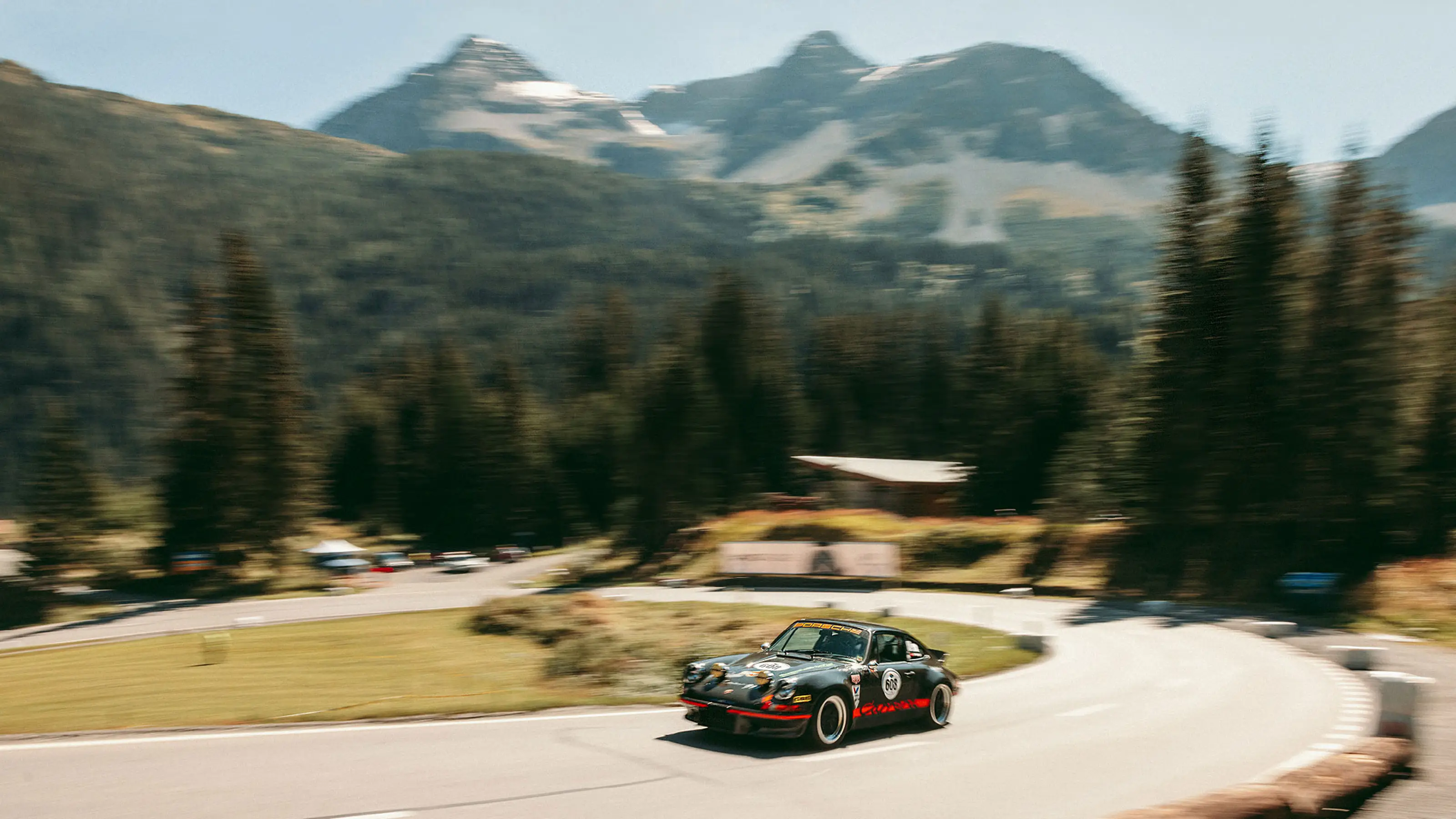 Voiture de sport classique sur route de montagne sinueuse avec montagnes boisées en arrière-plan.
