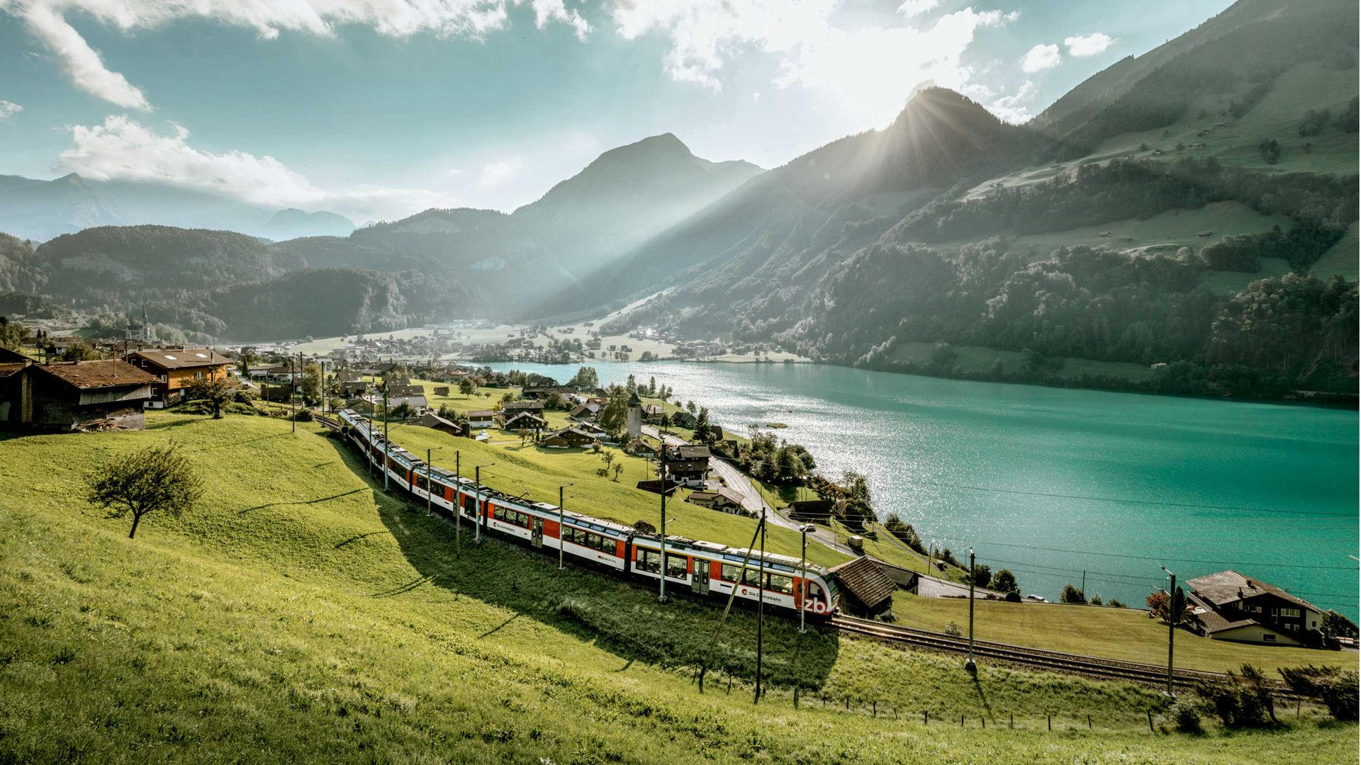 Ein Zug, der durch die Berge in der Nähe eines Sees fährt.