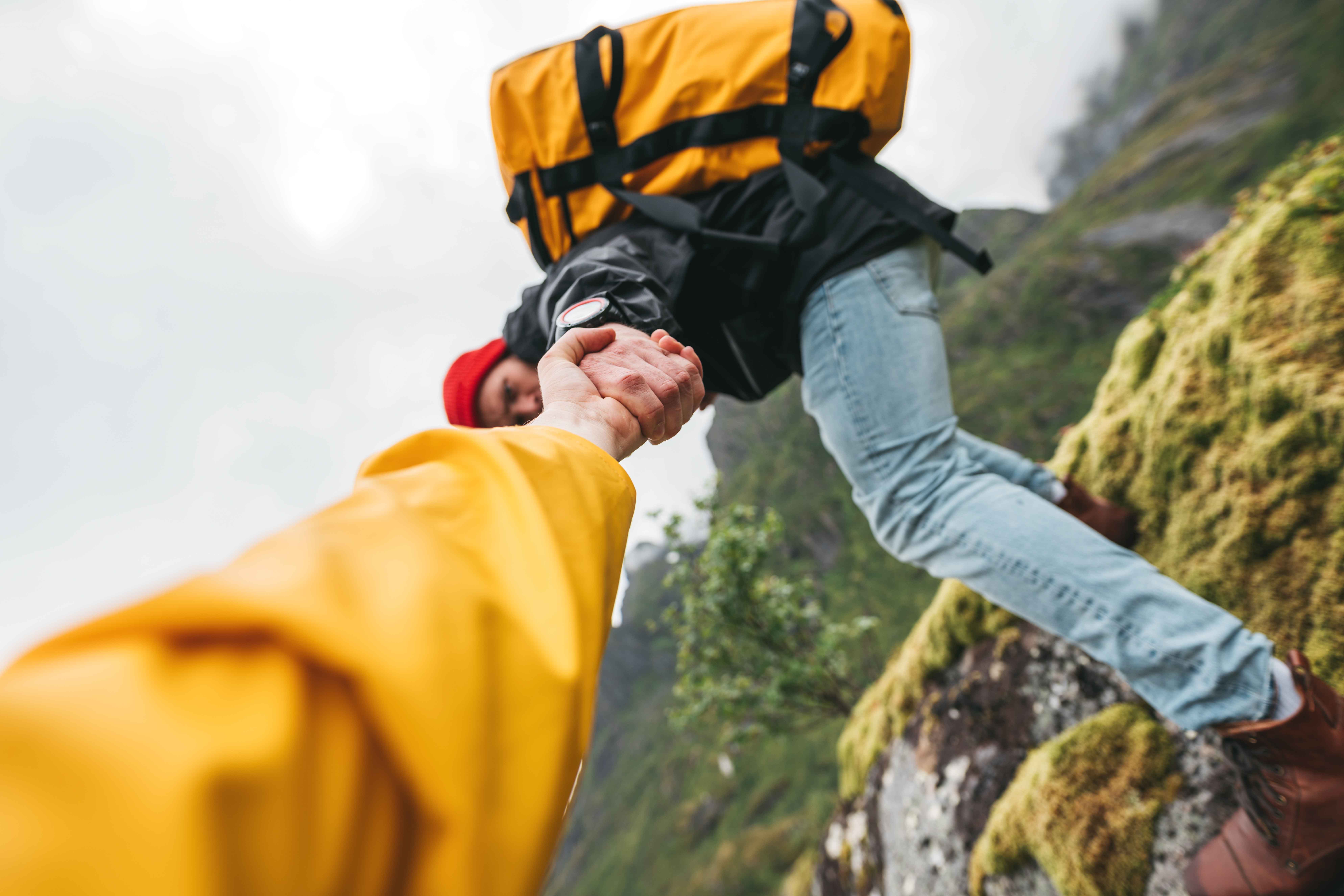 A person walks on a mountain trail, gripping a backpack, surrounded by scenic views of nature and rugged terrain.